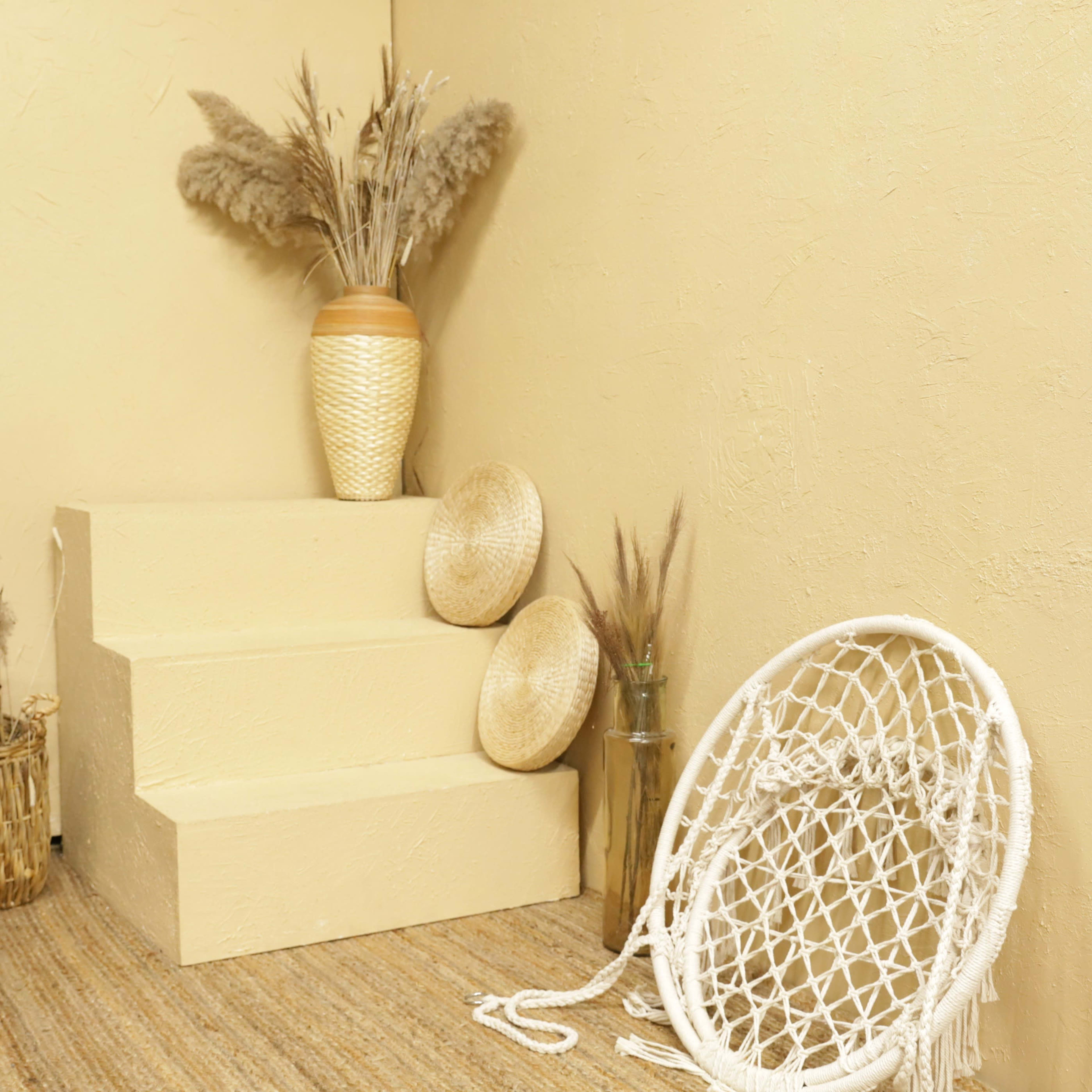 A warm-toned room with textured walls, a set of three steps, decorative vases, dried plants, and woven items arranged neatly.