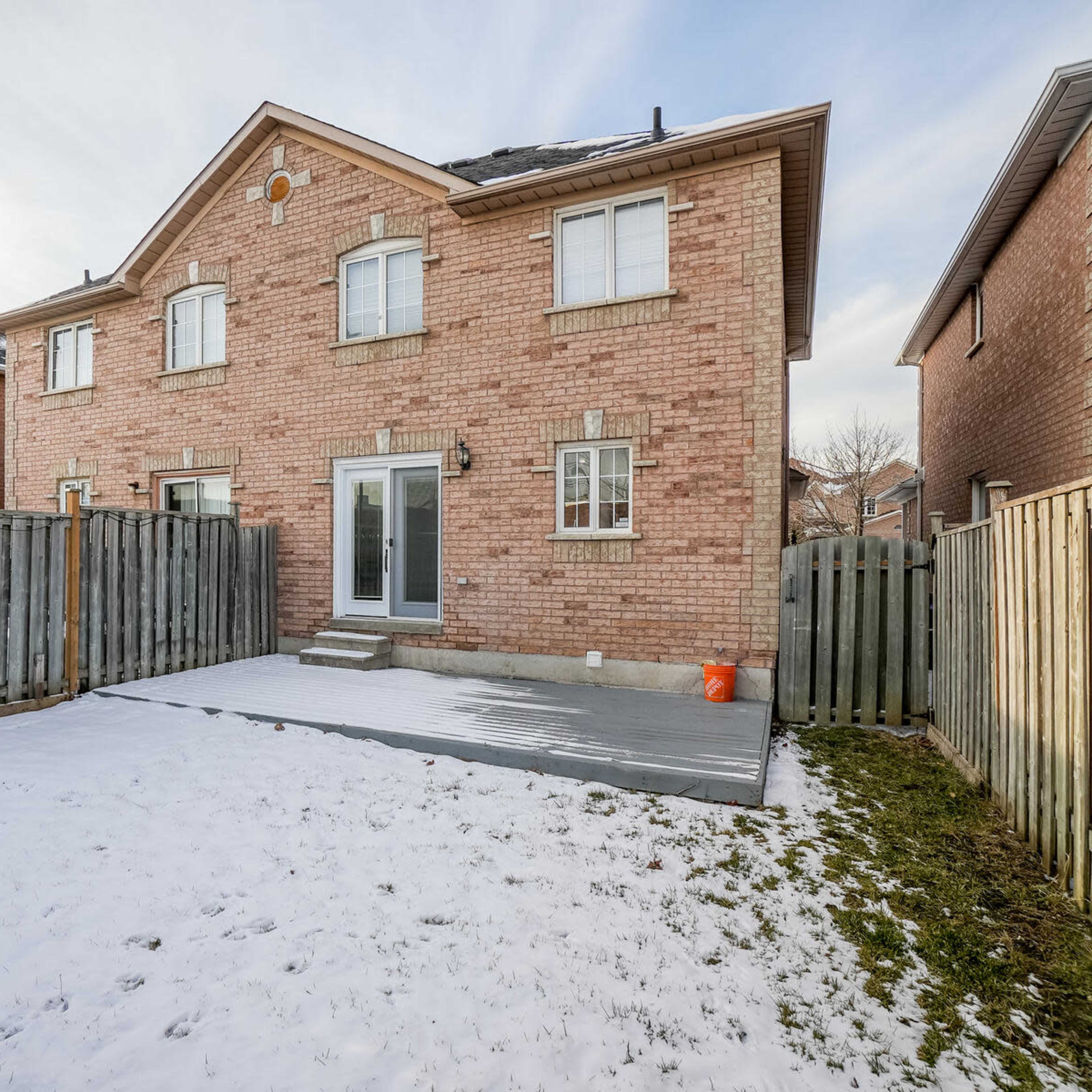 A two-story brick house with a partially snow-covered backyard and a wooden fence surrounding the property.