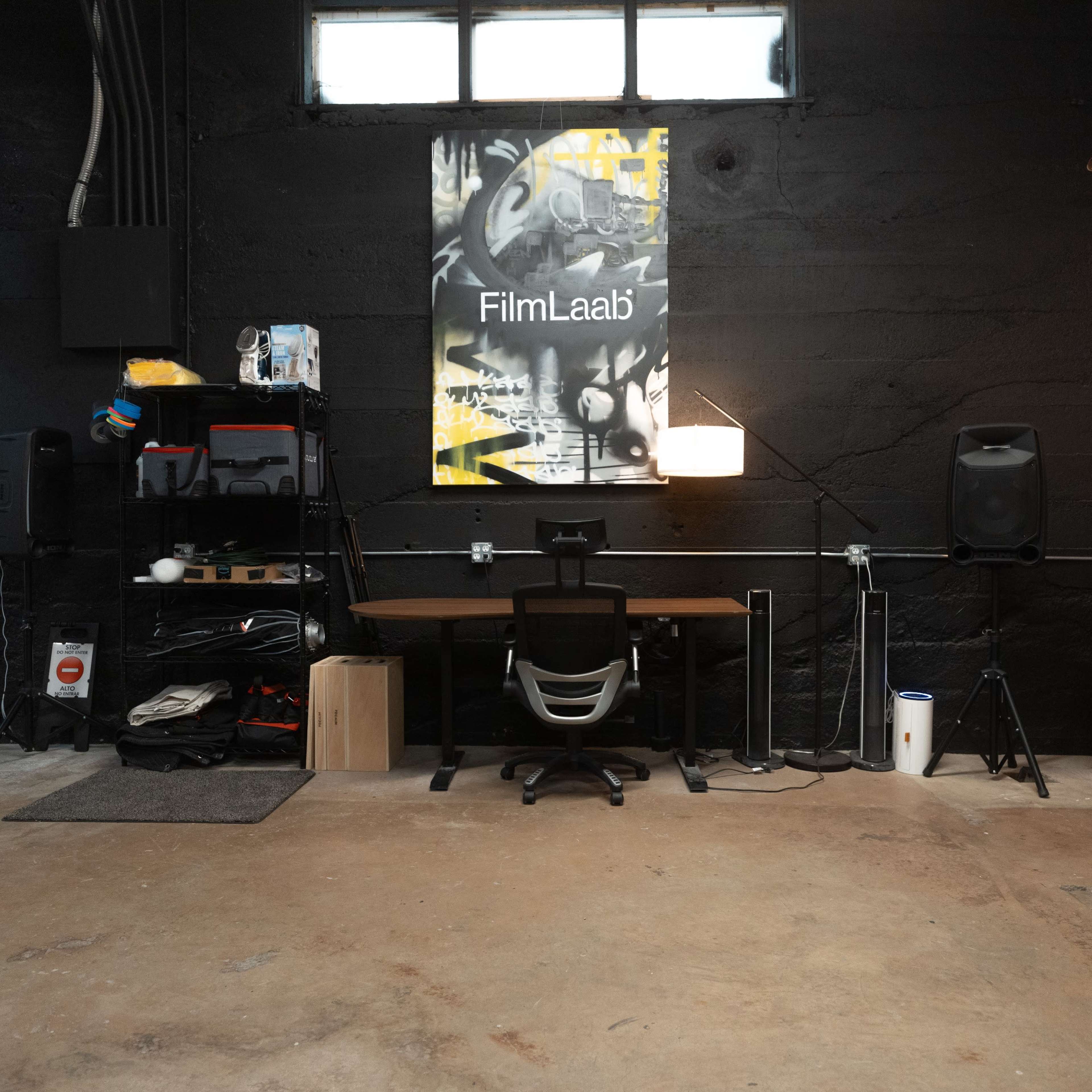 A workspace with a desk, chair, and various equipment against a black wall featuring a poster labeled "FilmLaab."