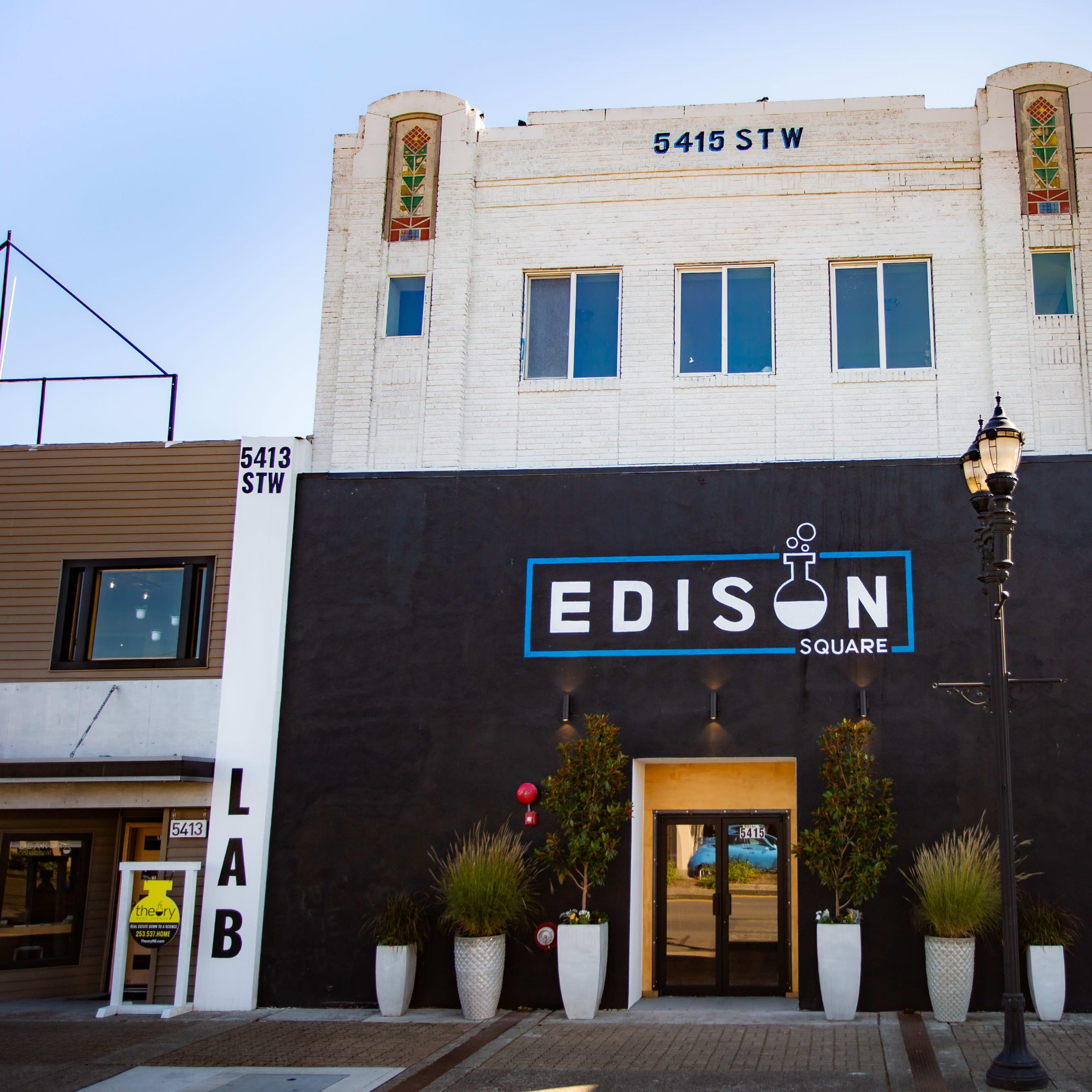 A historic building with the sign "EDISON SQUARE" prominently displayed on its front, flanked by planters and featuring a mix of architectural styles.