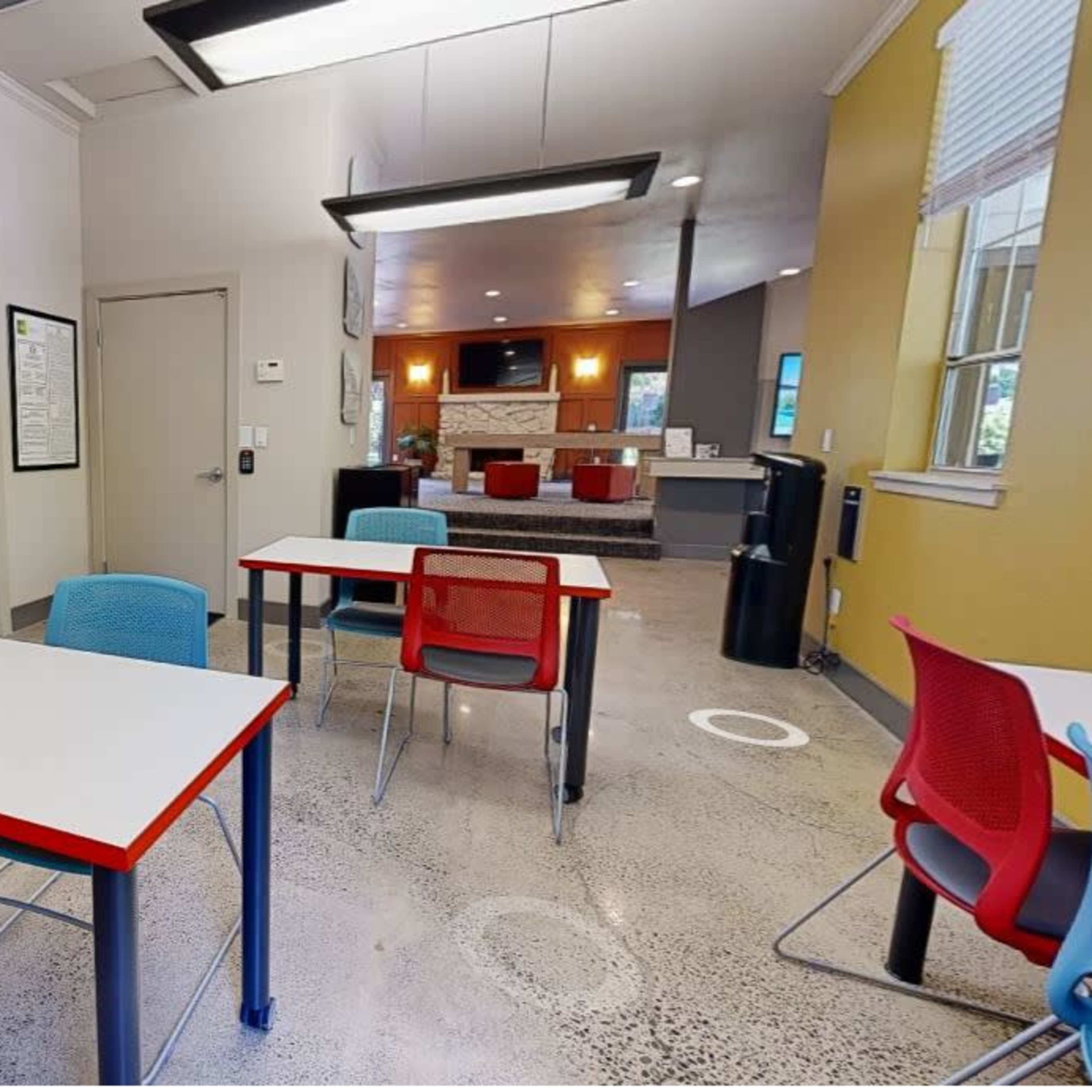 A well-lit room featuring several tables with colorful chairs arranged on a polished concrete floor.