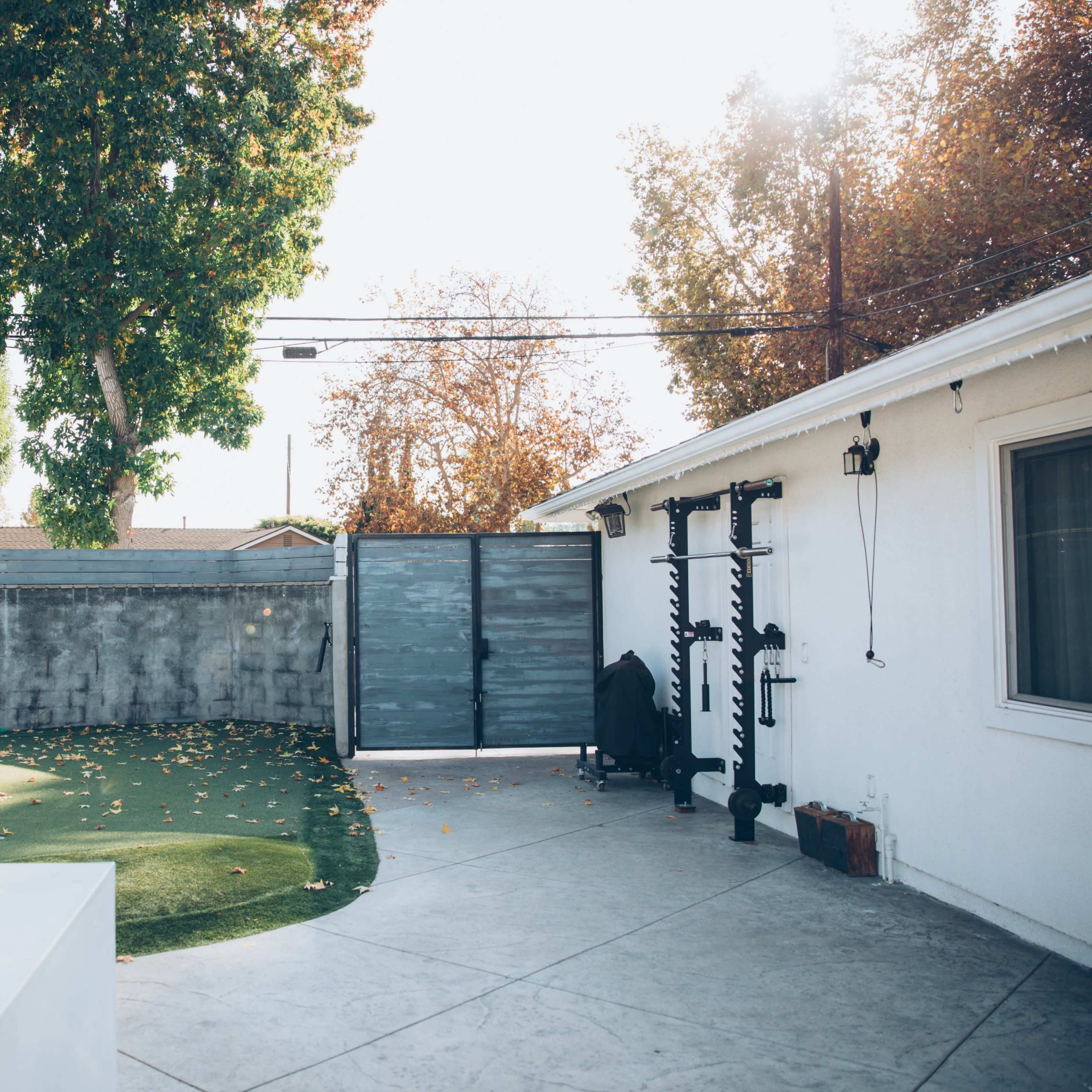 A backyard with artificial grass, a concrete patio, a gray fence, and trees in the background.