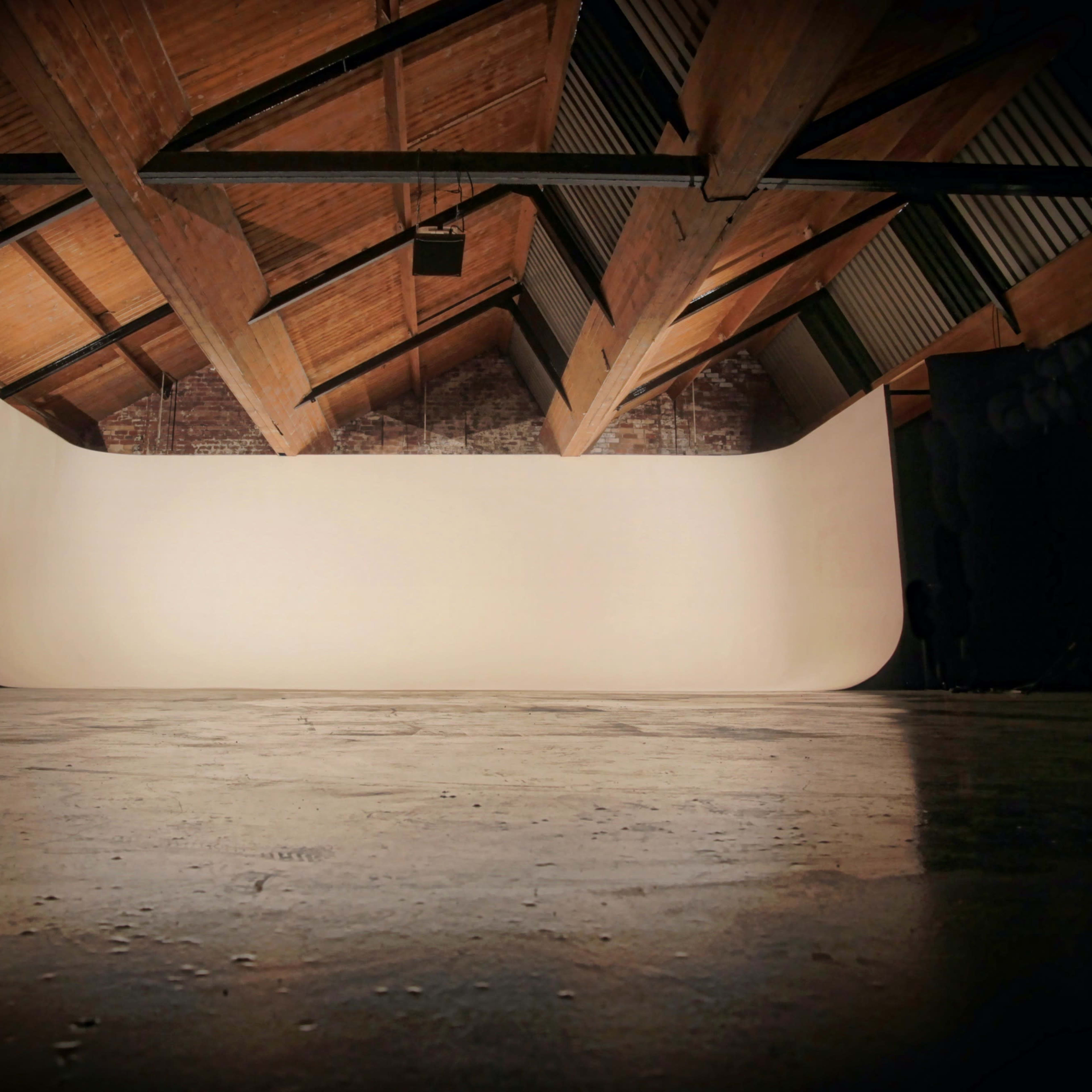 A spacious, empty studio with a curved backdrop and wooden beams overhead.