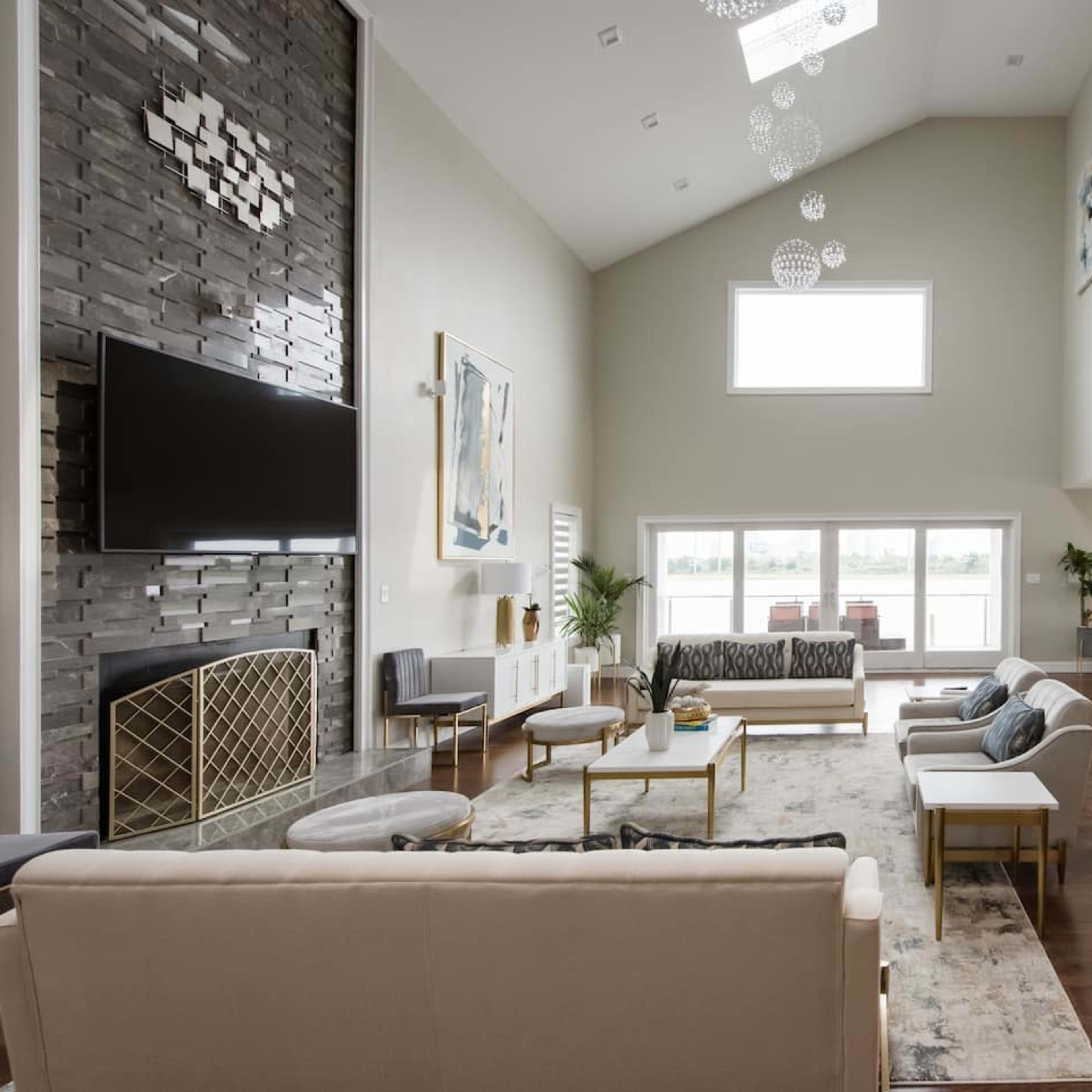 The scene features a spacious living room with high ceilings, large windows, and modern furnishings arranged around a fireplace and a central area rug.
