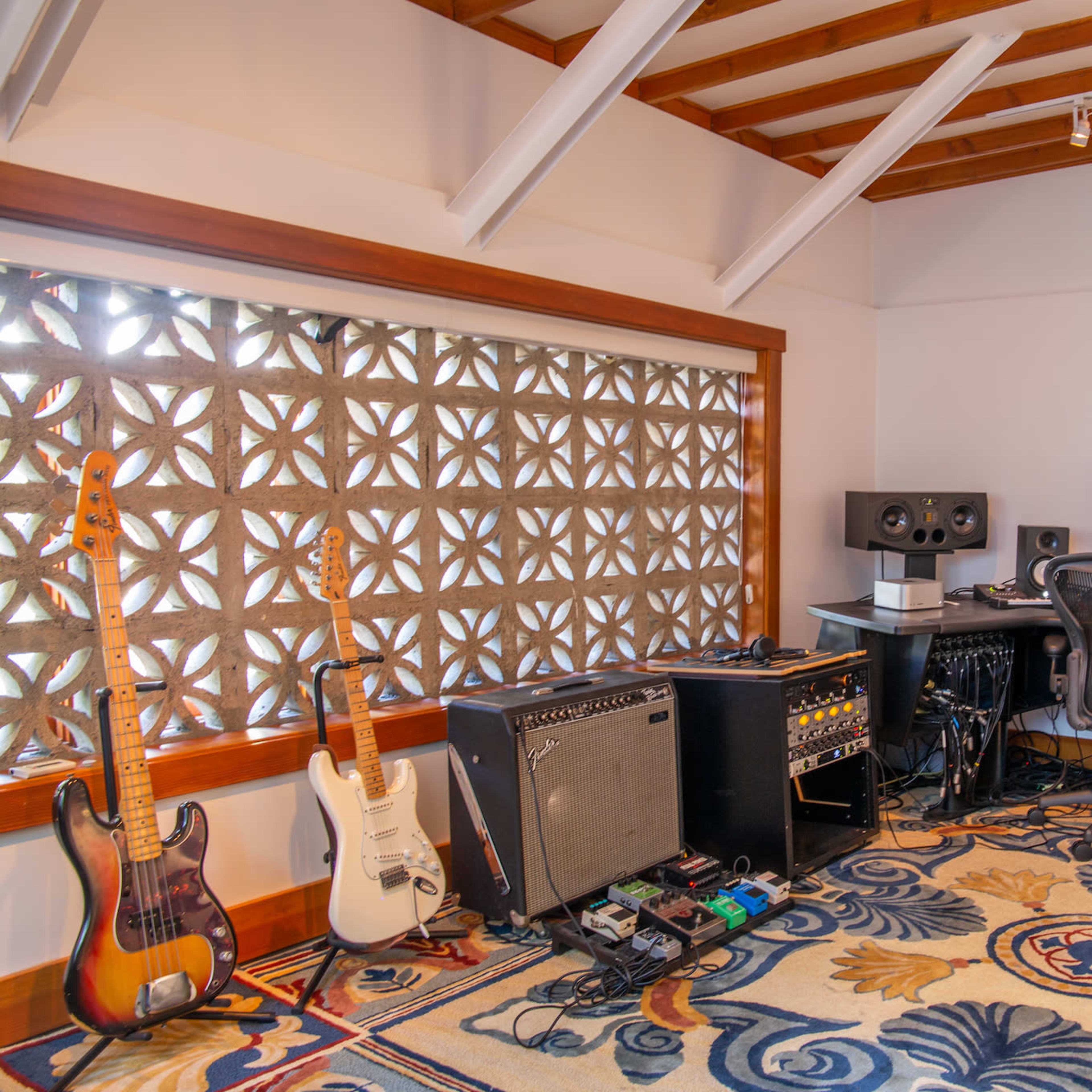 A music production studio with guitars, amplifiers, and a computer setup, featuring a decorative window.