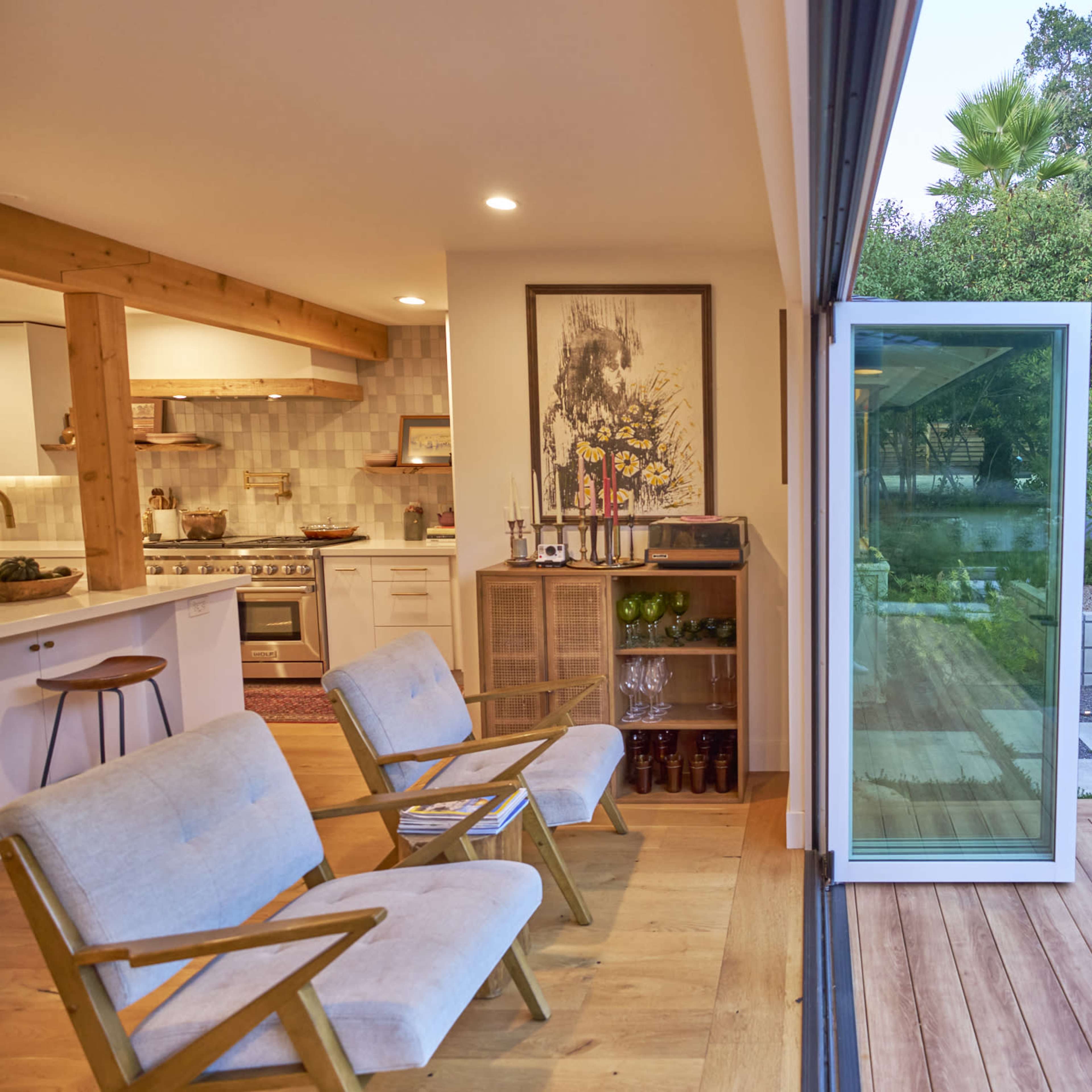 A modern kitchen and living area open up to a landscaped garden featuring pathways and greenery.