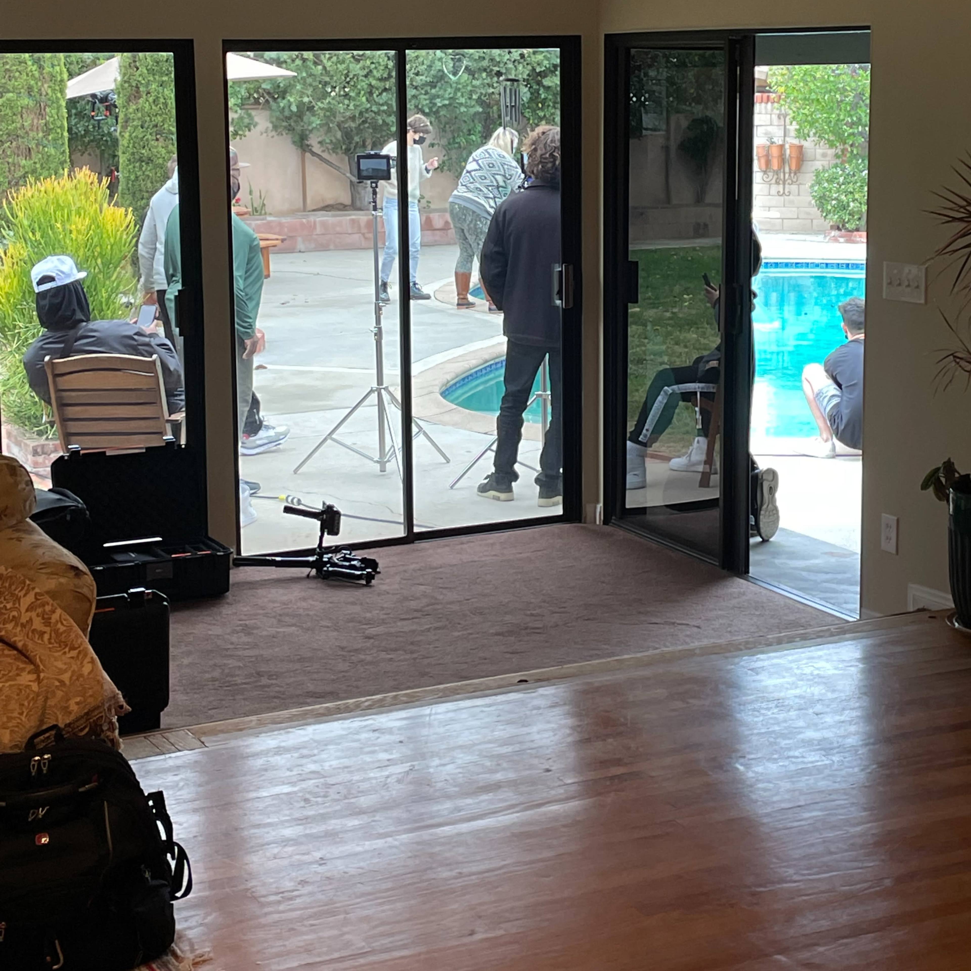 A group of people is gathered by a pool outside a house, with equipment set up nearby.