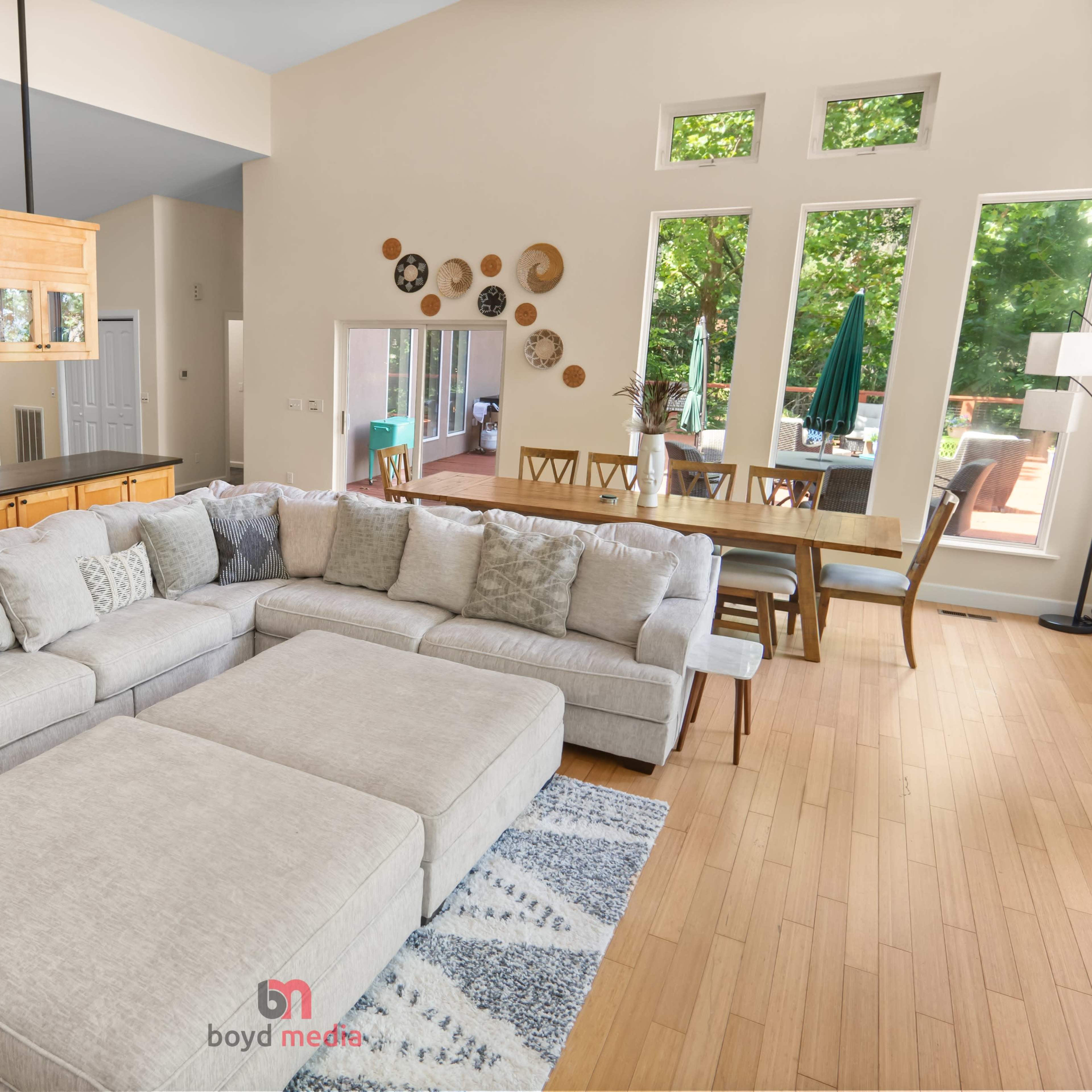 A spacious living room features a large sectional sofa, a dining area with a table, and large windows allowing natural light to fill the space.