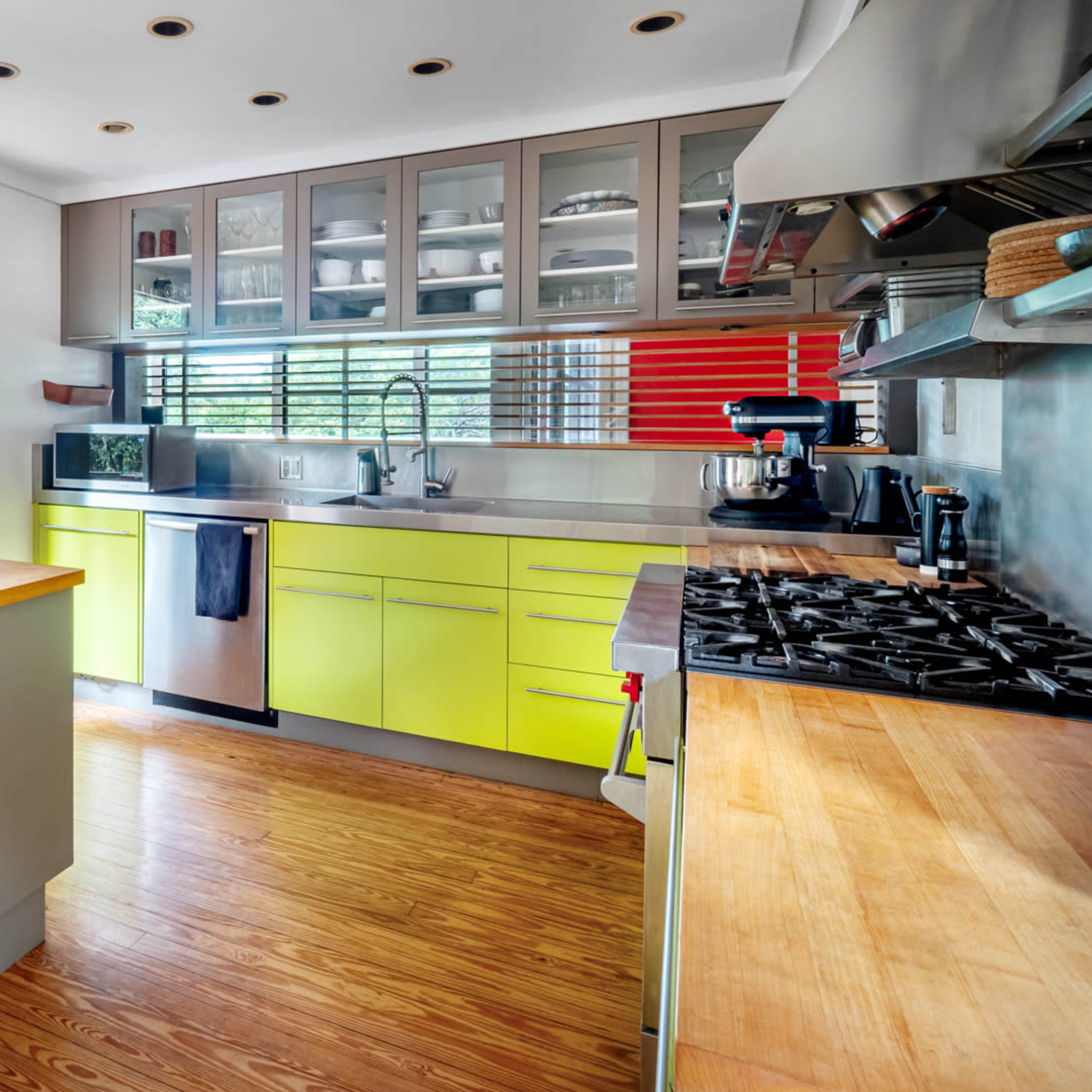A modern kitchen with a wooden island, lime green cabinetry, and a bookshelf integrated into the design.