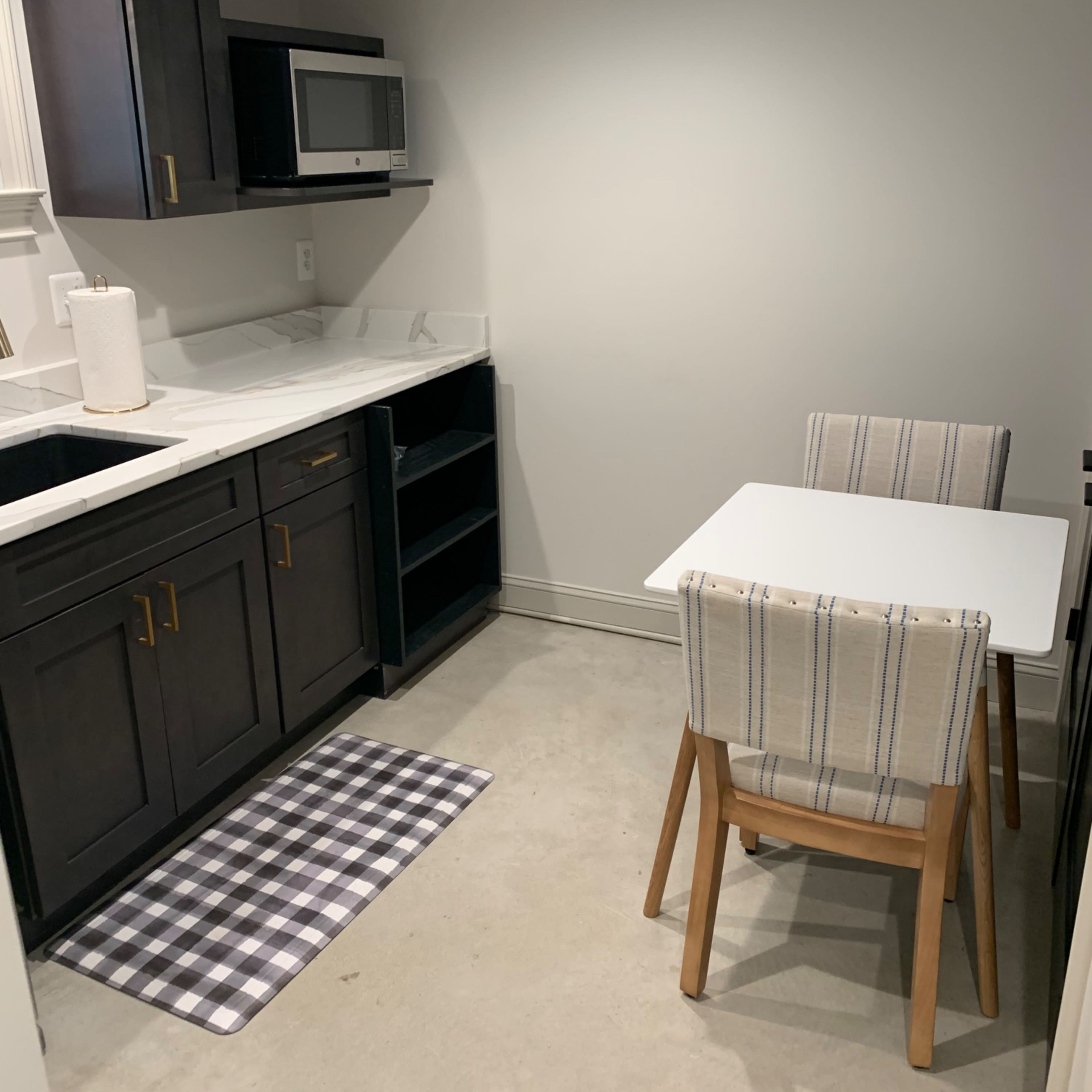 A compact kitchenette features dark cabinetry, a small dining table with two chairs, and a microwave on the counter.