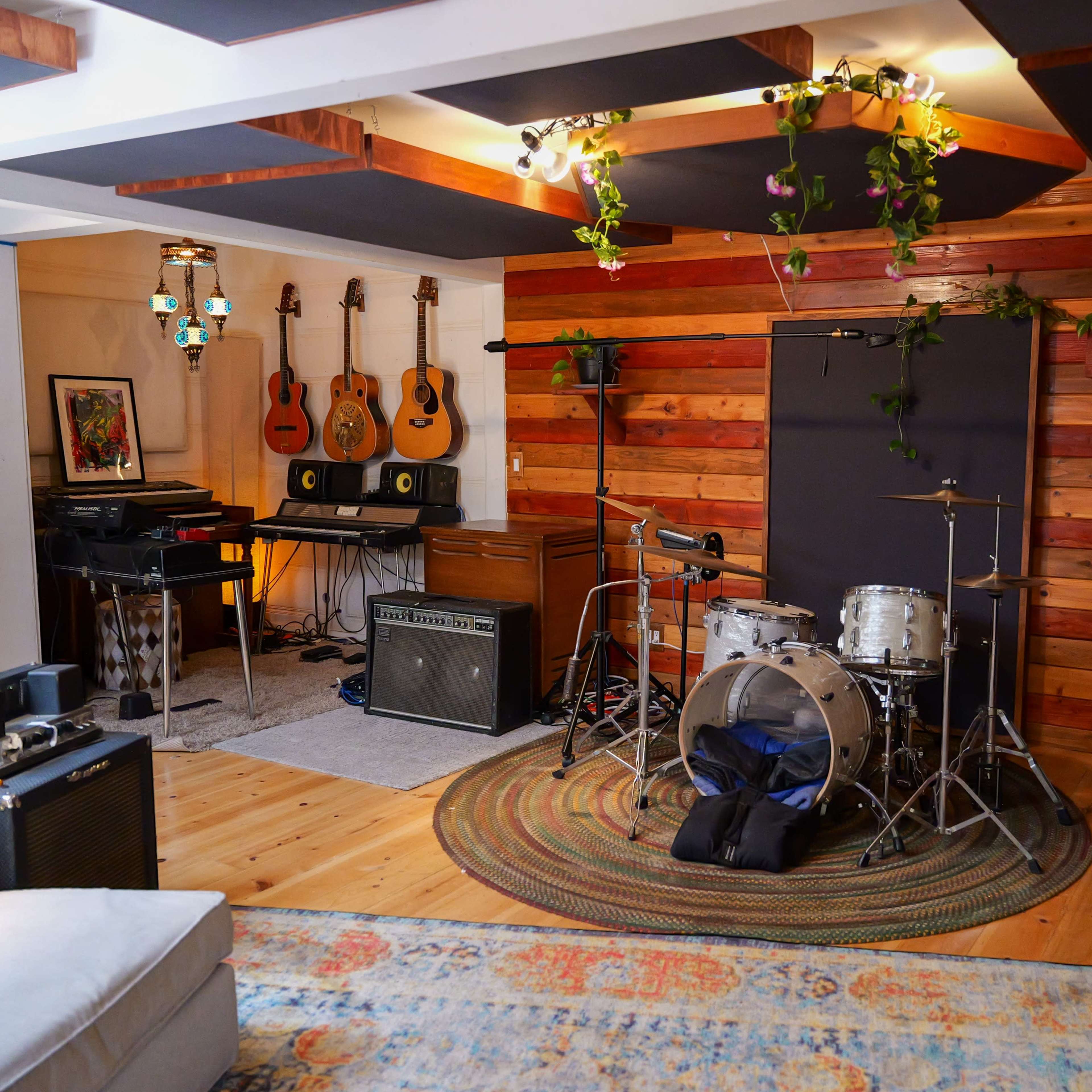 A music practice room featuring drums, guitars, keyboards, amplifiers, and decorative plants against wooden walls.