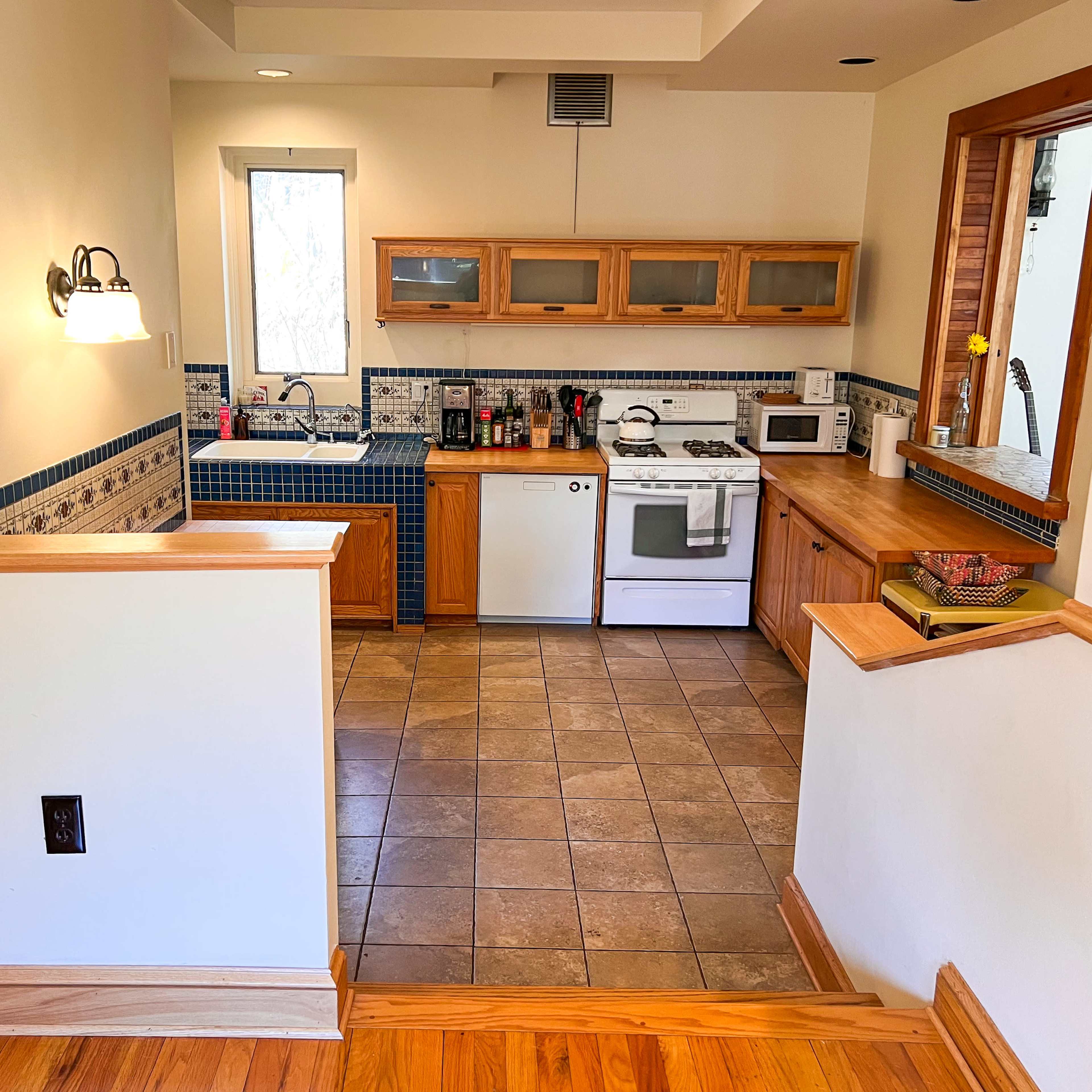A kitchen area with wooden cabinets, a tiled floor, and modern appliances, situated beside a staircase.