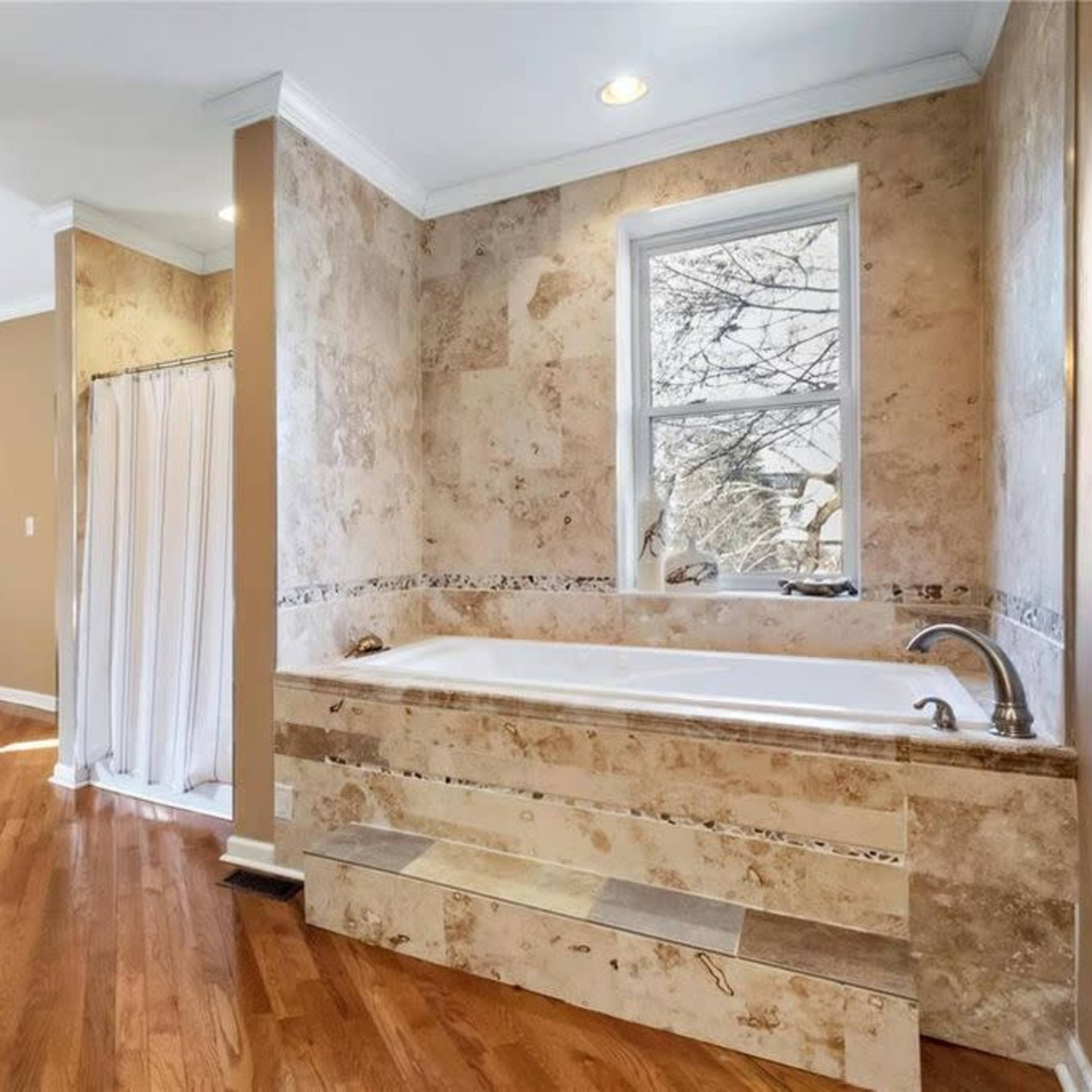 A bathroom featuring a large bathtub, a window with a view, and a wooden shelving unit against the wall.