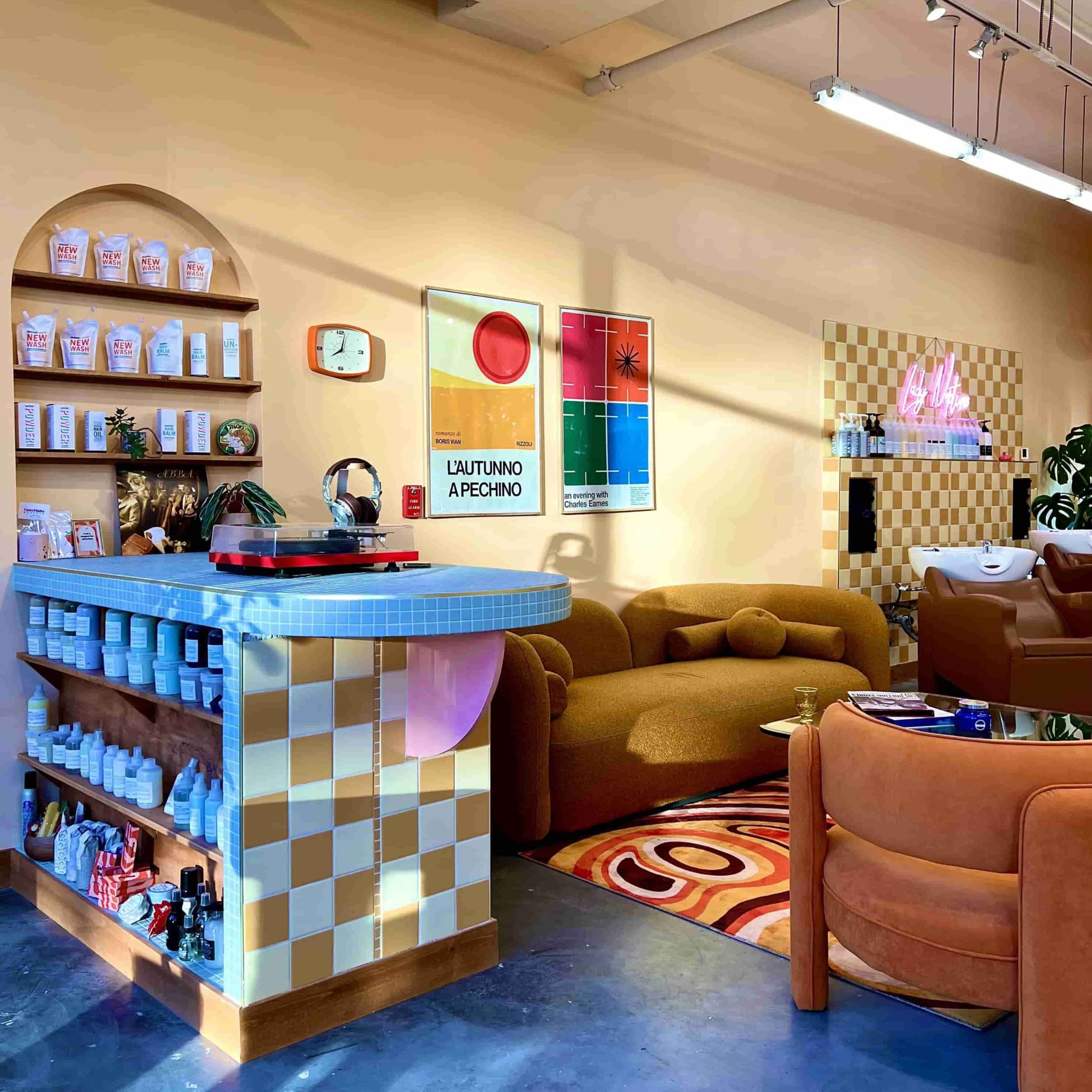 A brightly lit salon interior with a checkered counter, colorful wall art, and cozy seating areas.