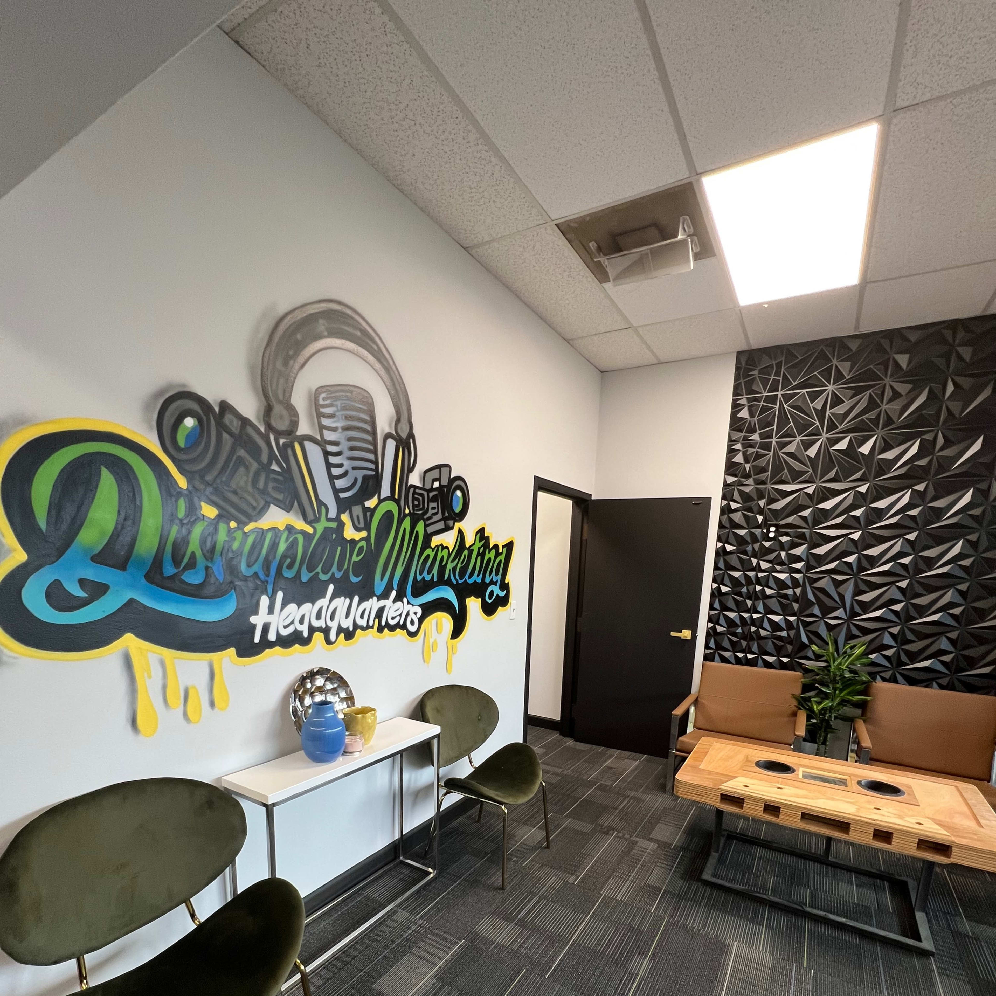A modern office space with a mural reading "Disruptive Marketing Headquarters," green chairs, a wooden coffee table, and a decorative plant.