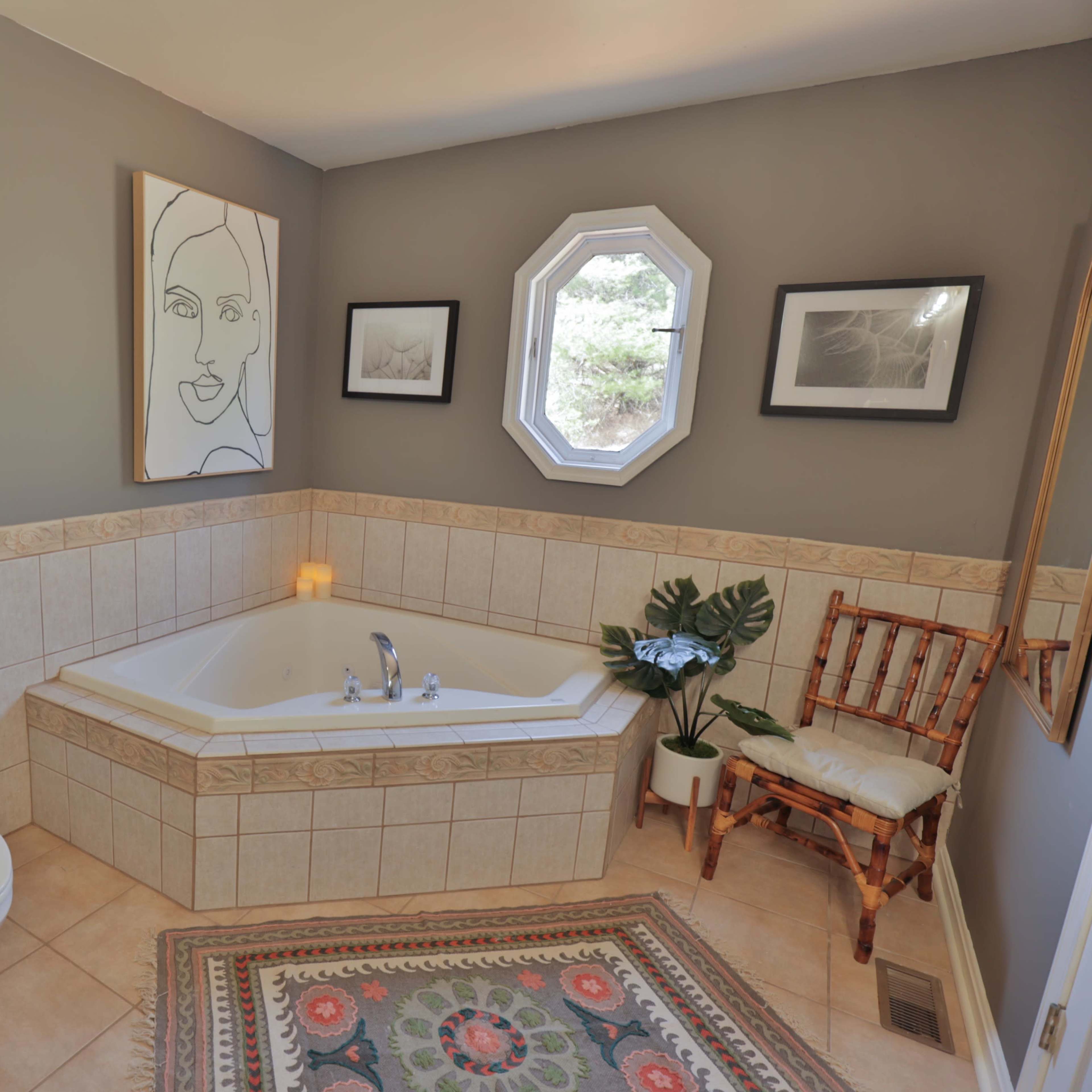A bathroom with a corner bathtub, a toilet, a decorative shelf with plants, and framed artwork on the walls.