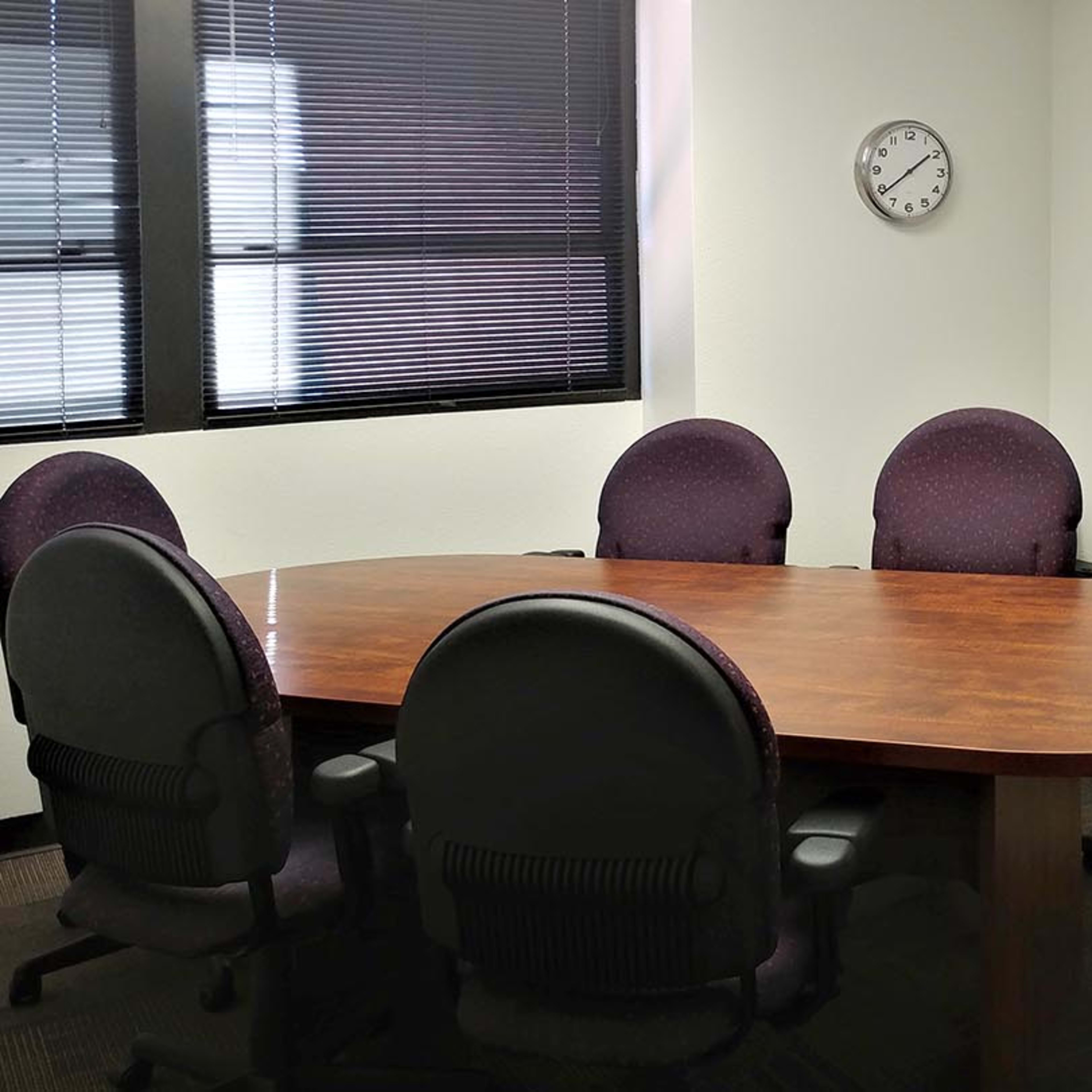 A large, oval wooden conference table surrounded by six purple upholstered chairs in a brightly lit meeting room.