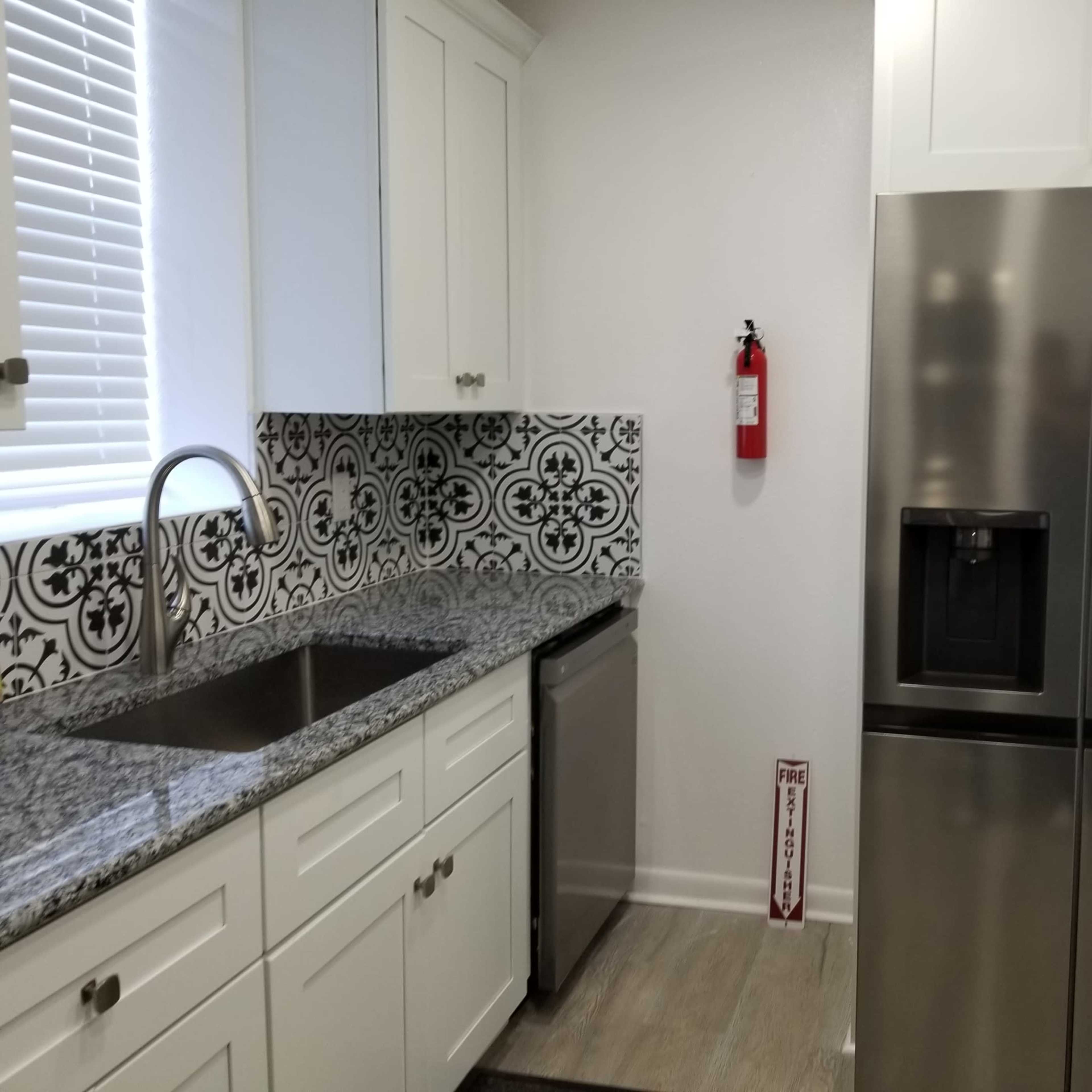 A kitchen with a stainless steel refrigerator, a countertop with a sink, and decorative tiles behind the sink.