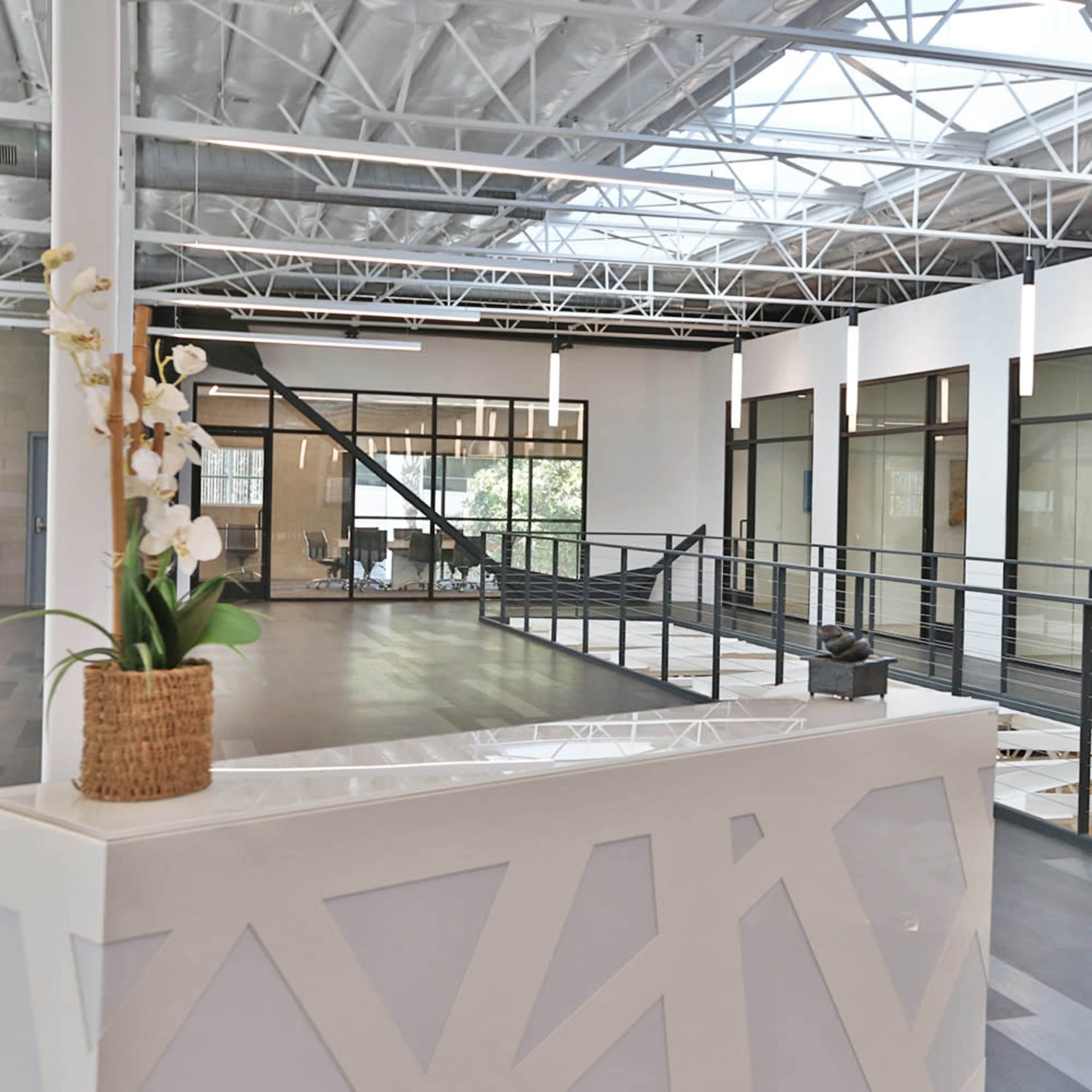 A modern office space with a reception area, large windows, and a balcony overlooking an open area below.