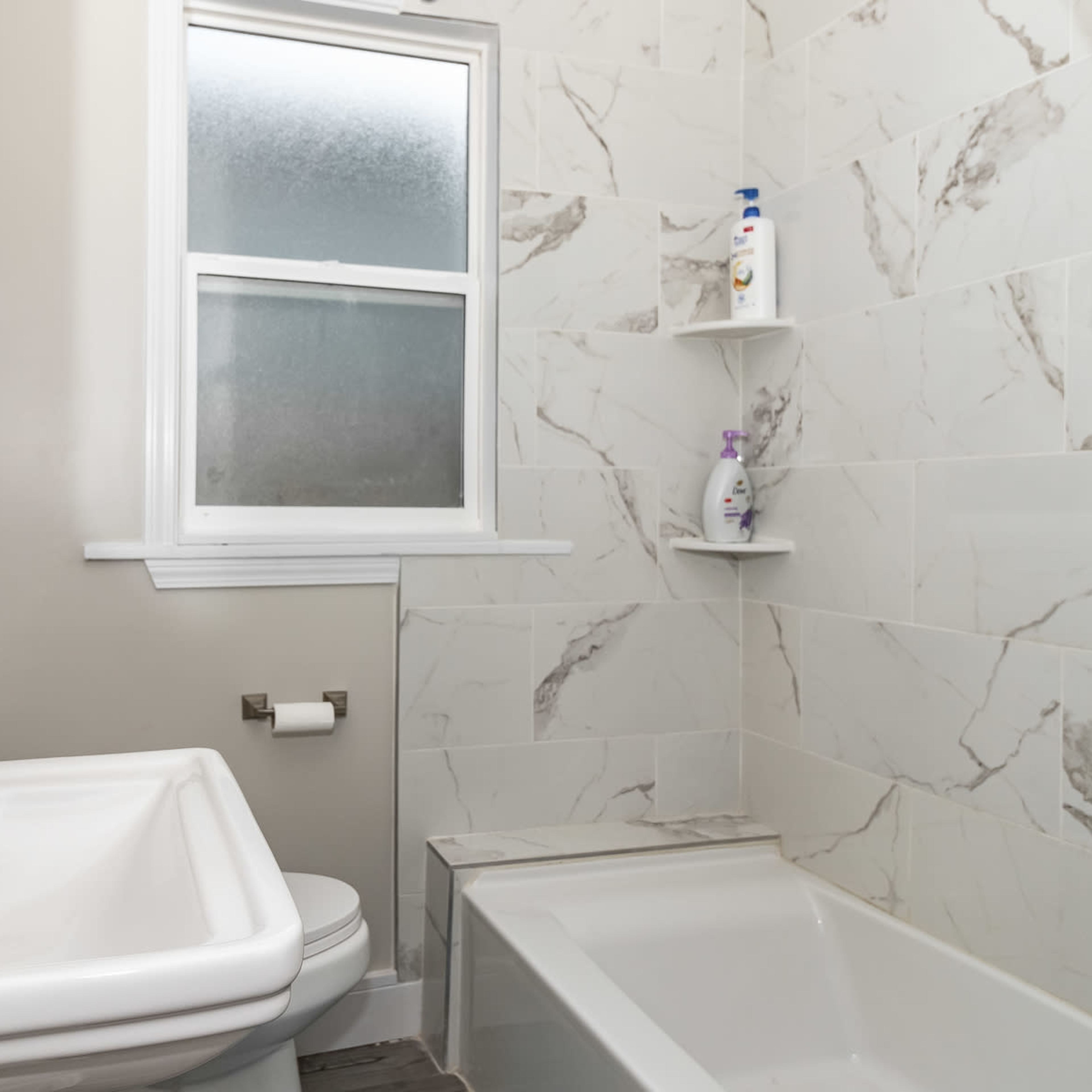A bathroom featuring a white sink, a toilet, and a tub with a marble-patterned tile surround.