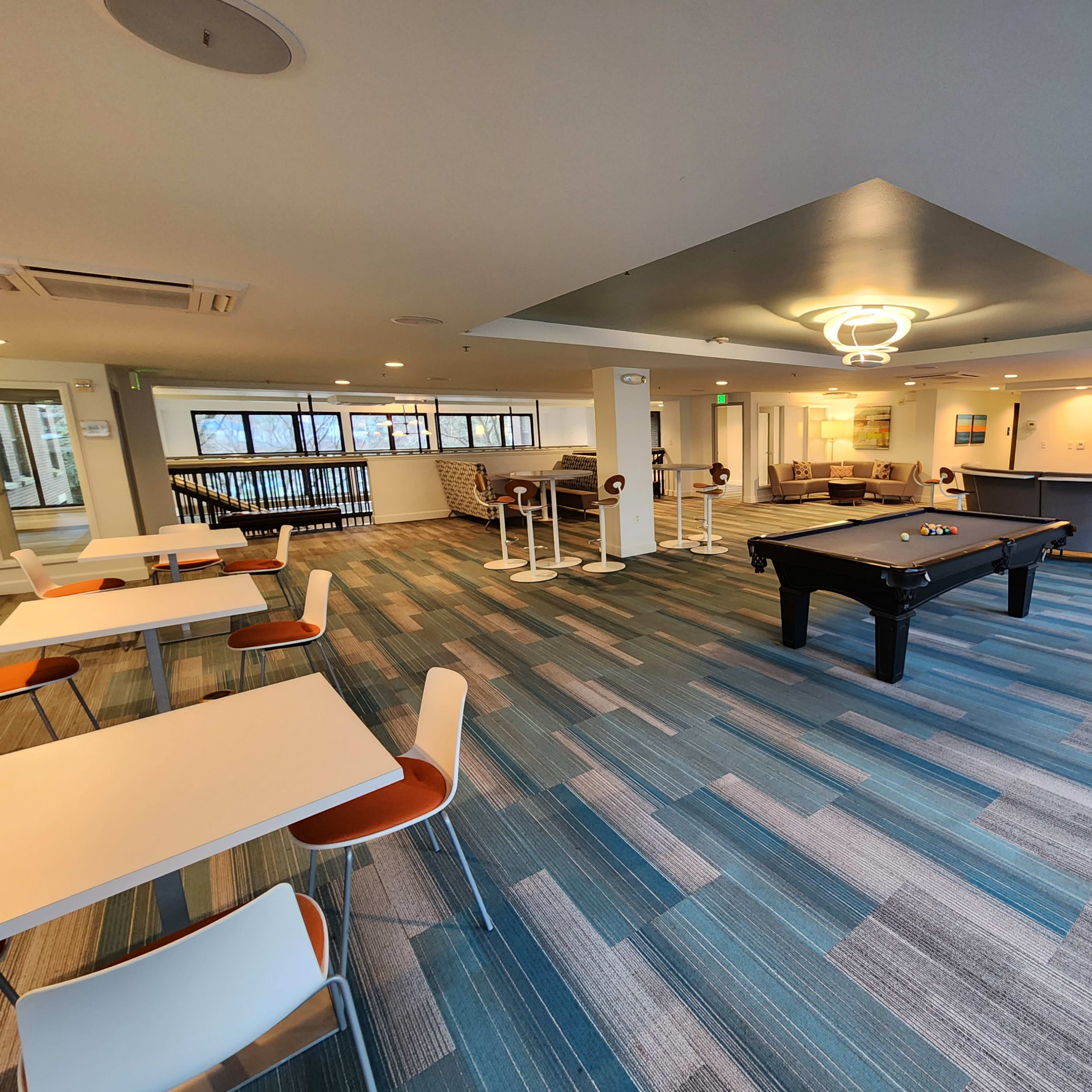 A lounge area featuring a pool table, several tables with chairs, and a seating area with modern furnishings.