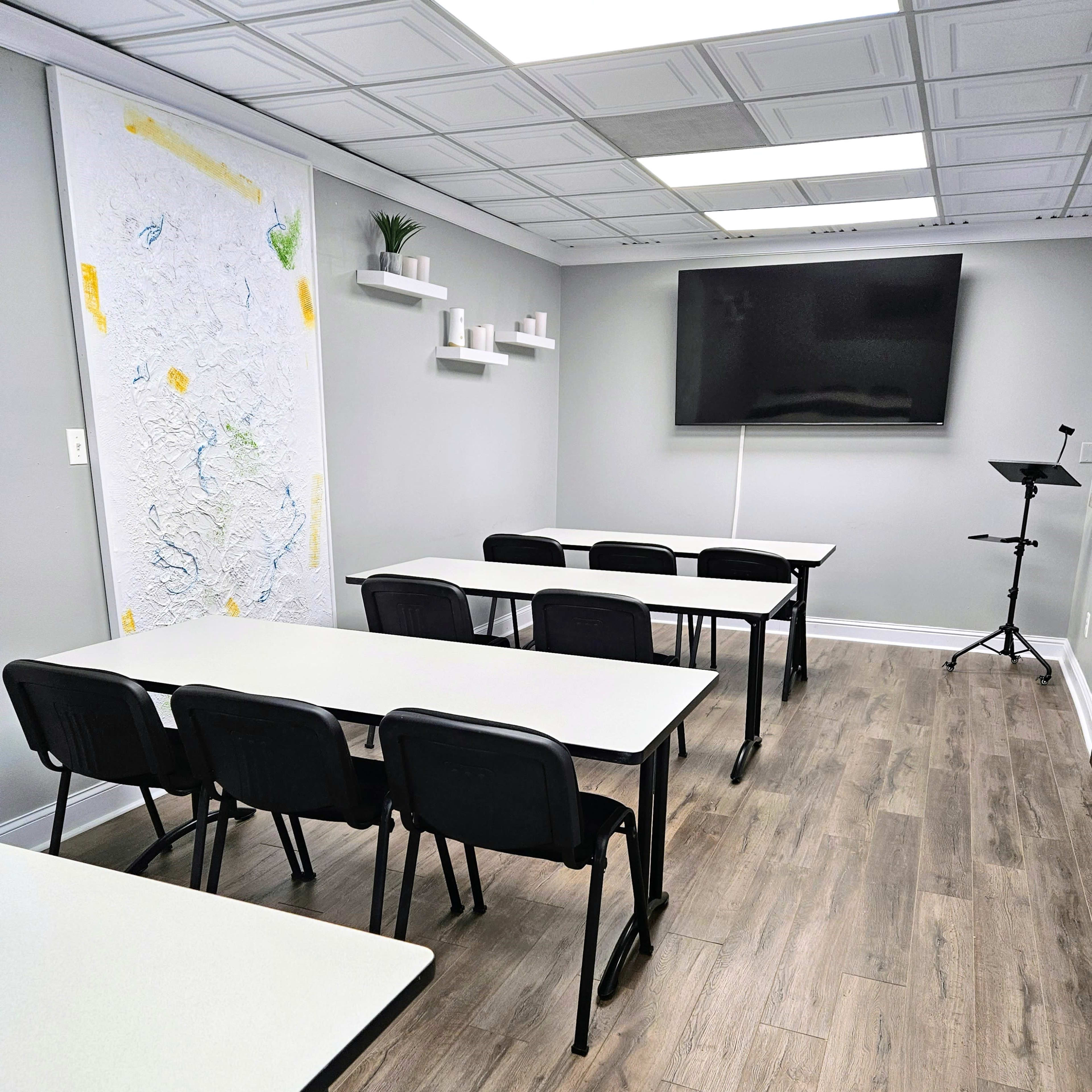A modern classroom setup with rows of white tables and black chairs, a large screen on the wall, and minimalistic decor.