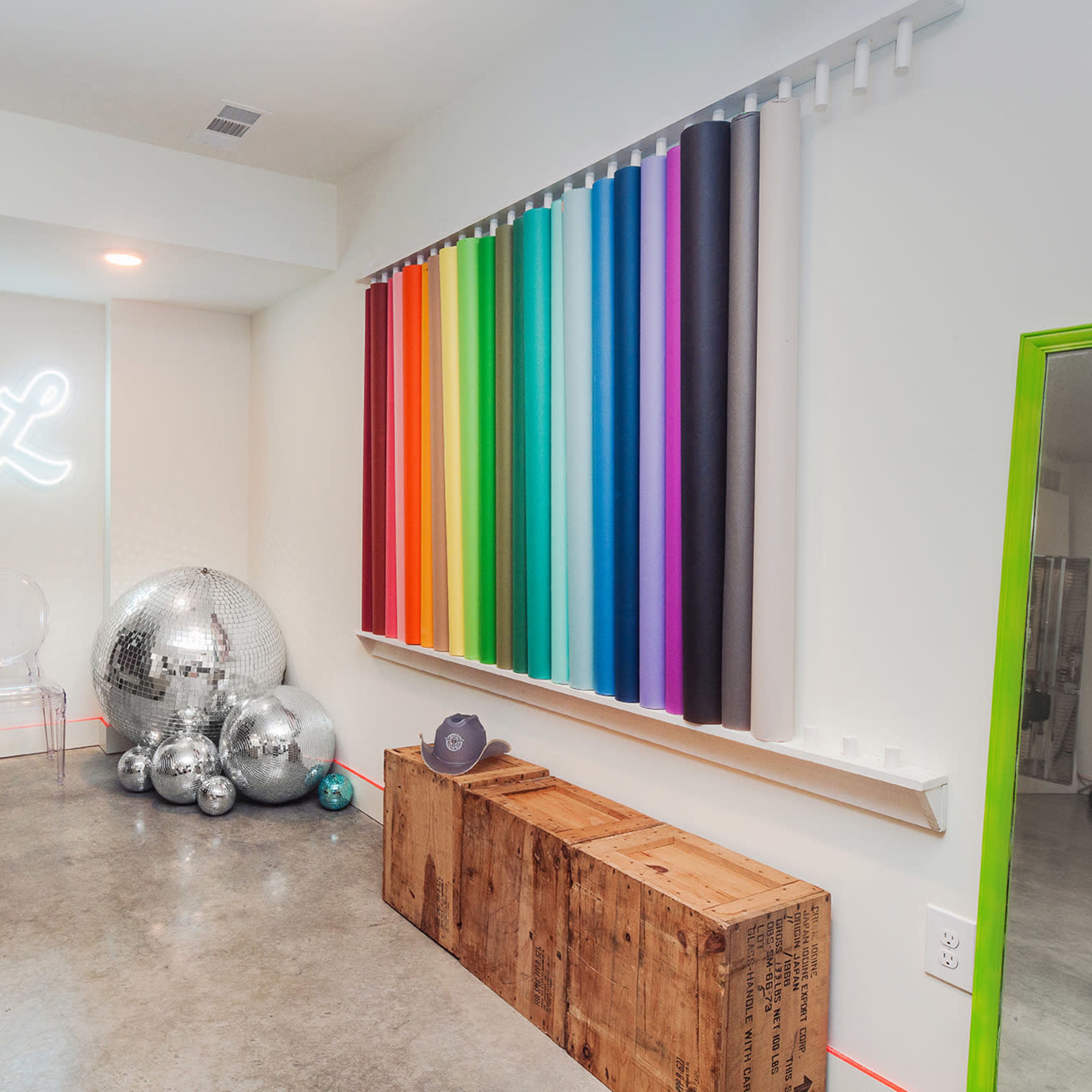 A brightly colored interior space featuring a yellow sofa, a wall with various colored vertical stripes, and shiny disco balls arranged near a wooden crate.