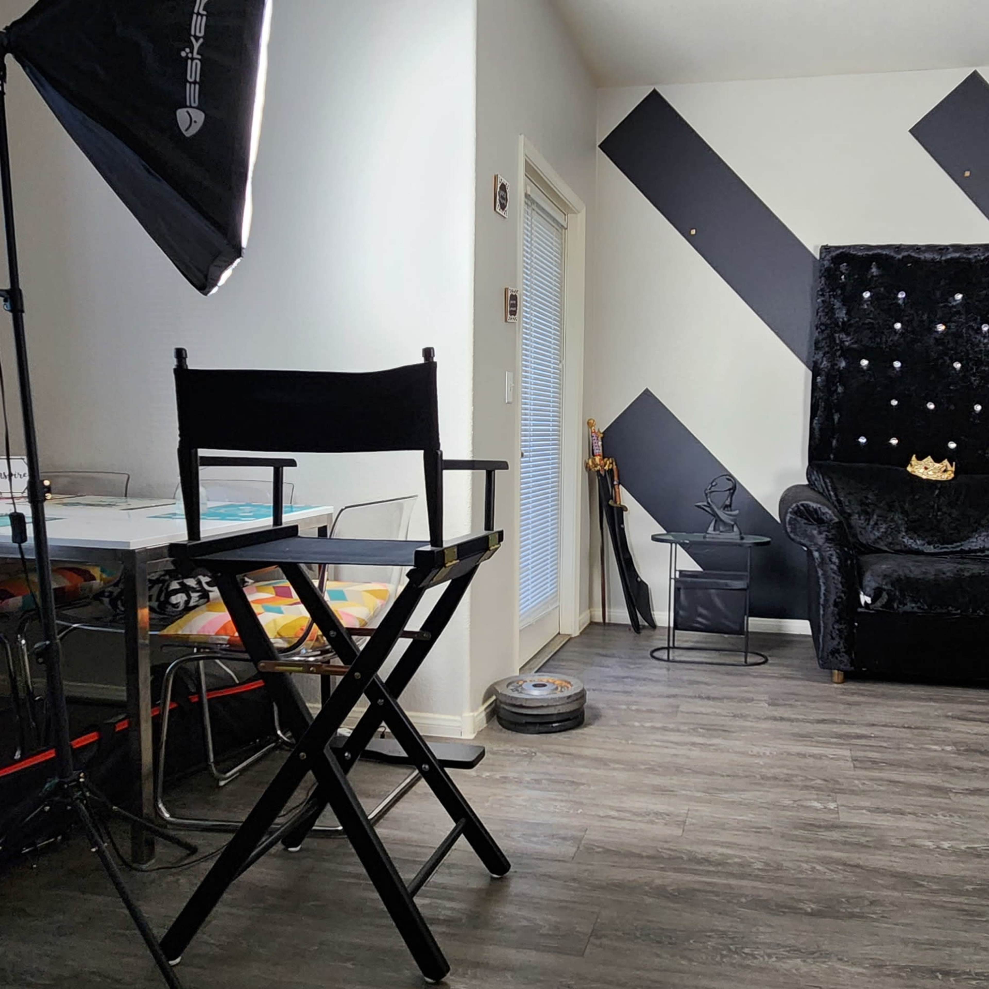 A brightly lit room featuring a black velvet chair, a glass table, and two photographic lighting setups.