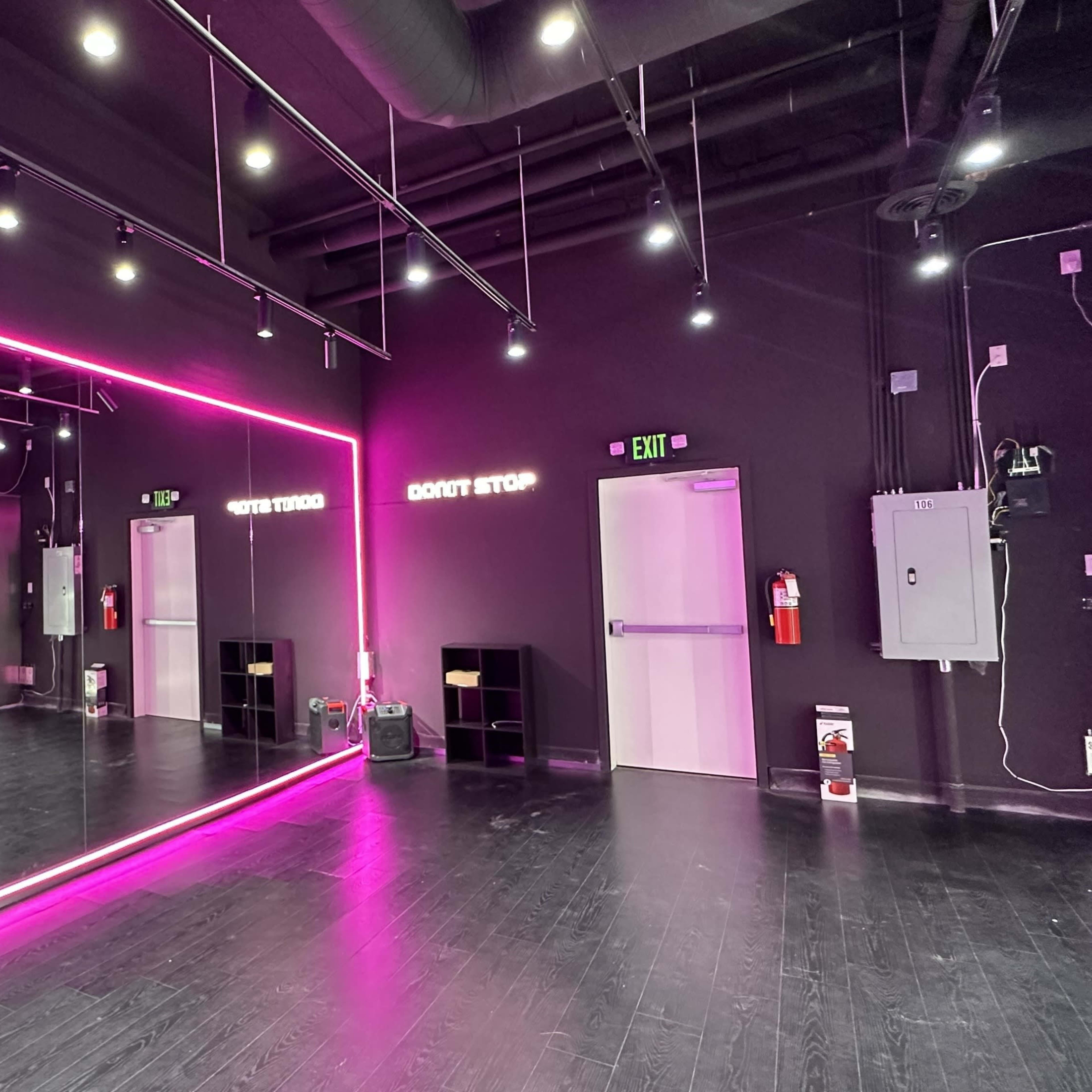 A modern dance studio with black walls, pink neon lighting, and large mirrors.