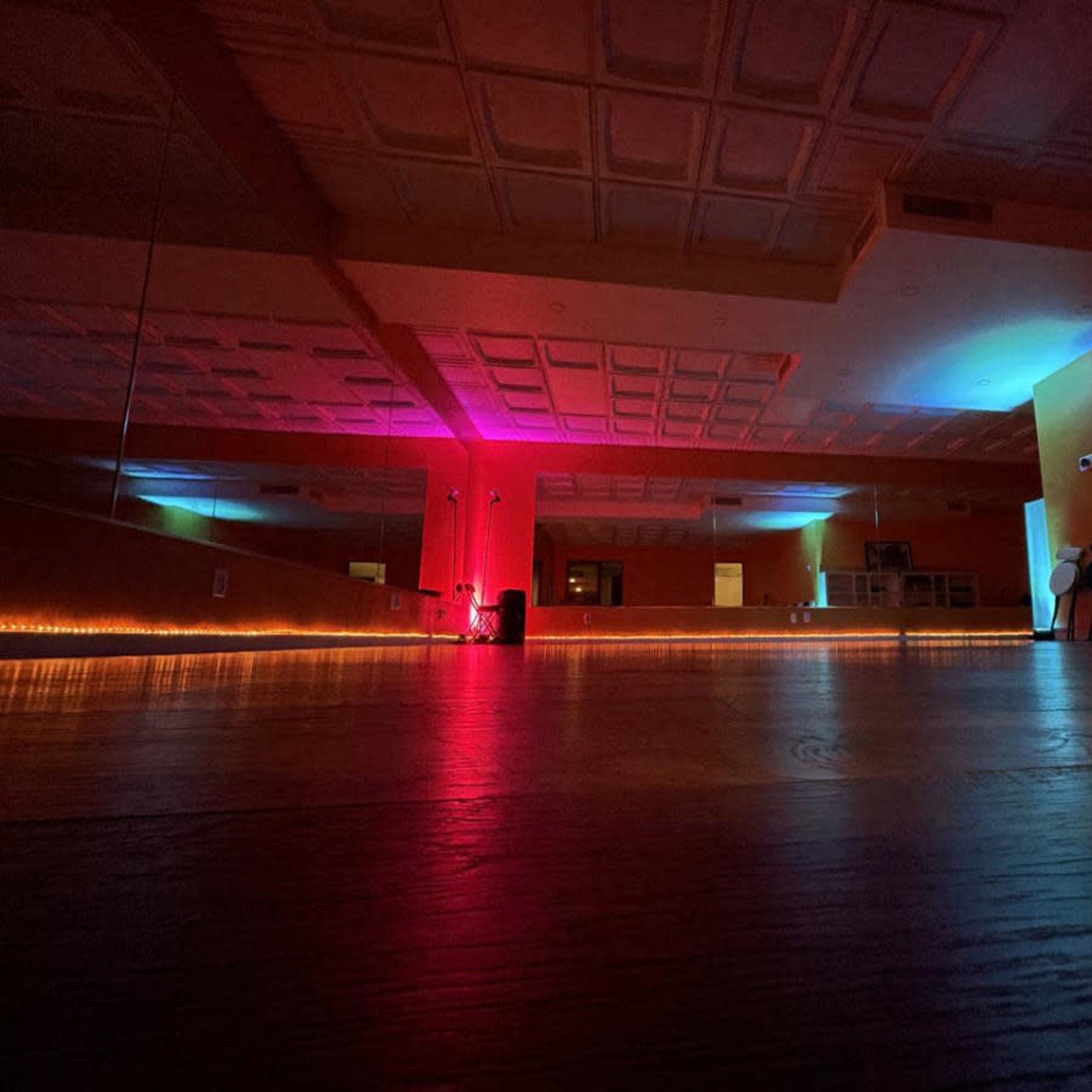 A spacious room with colorful lighting along the walls and a row of chairs against one side.