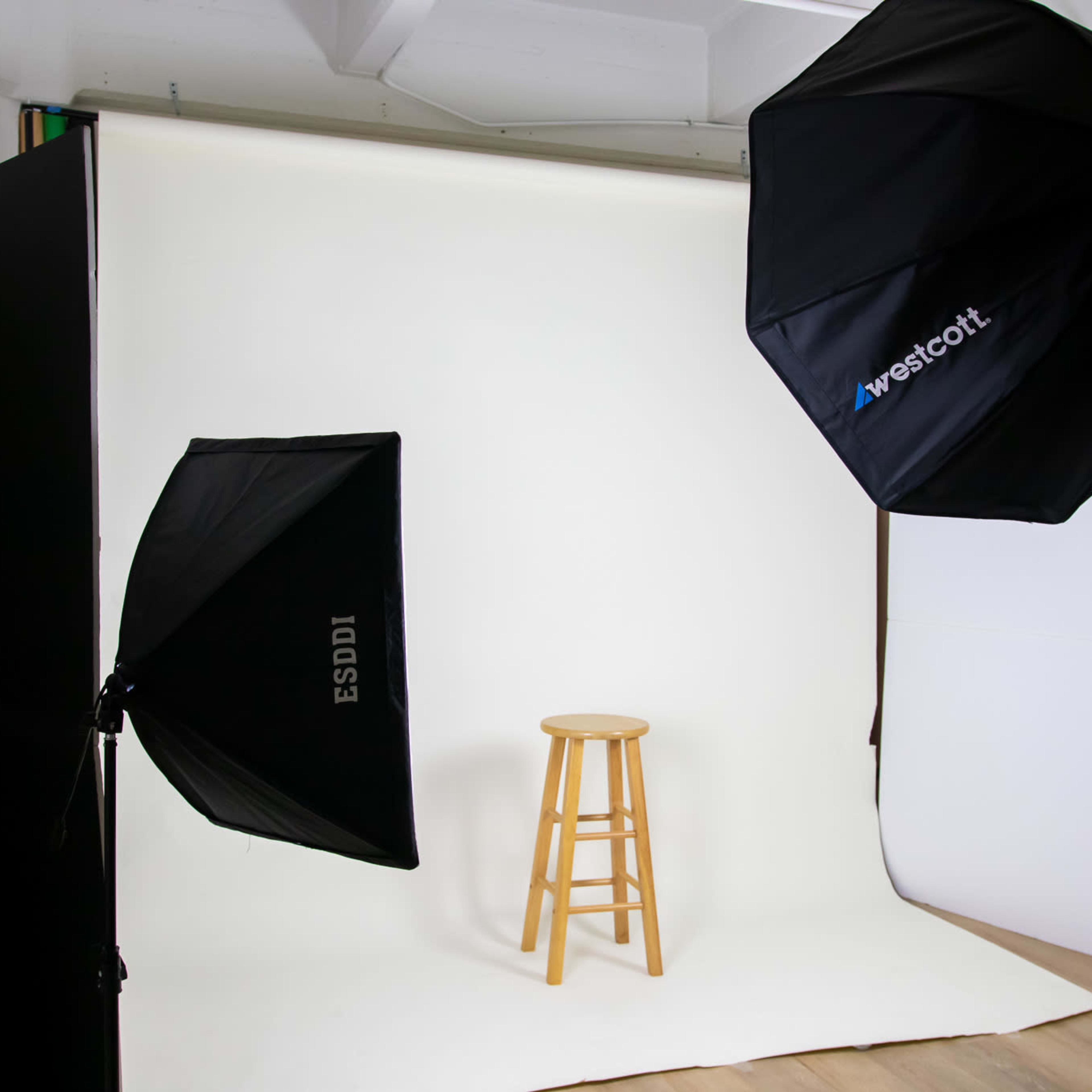 A photography studio setup with two softbox lights positioned on either side of a wooden stool against a seamless backdrop.