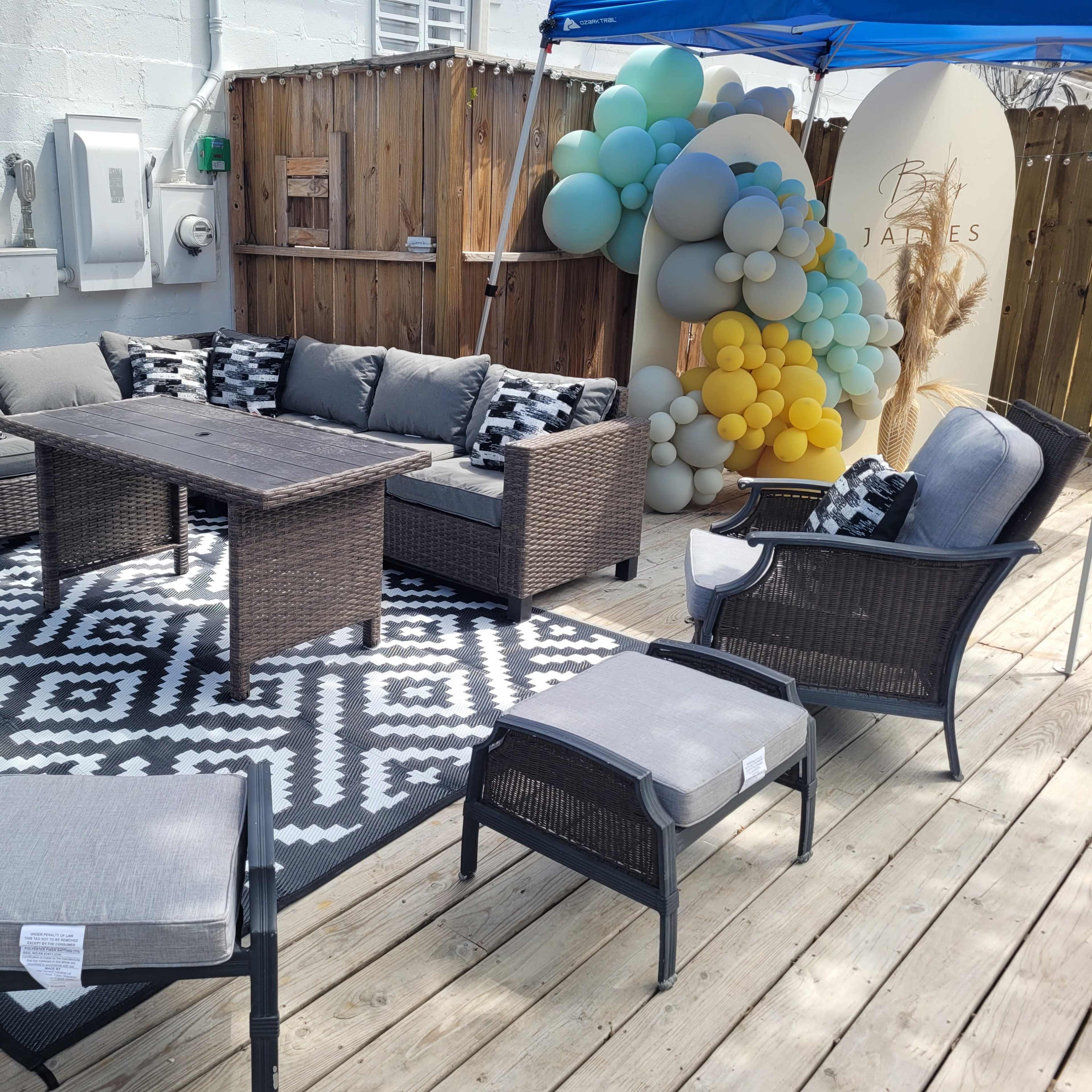 A stylish outdoor seating area features a sectional sofa, a coffee table, and several additional chairs arranged on a geometric-patterned rug.