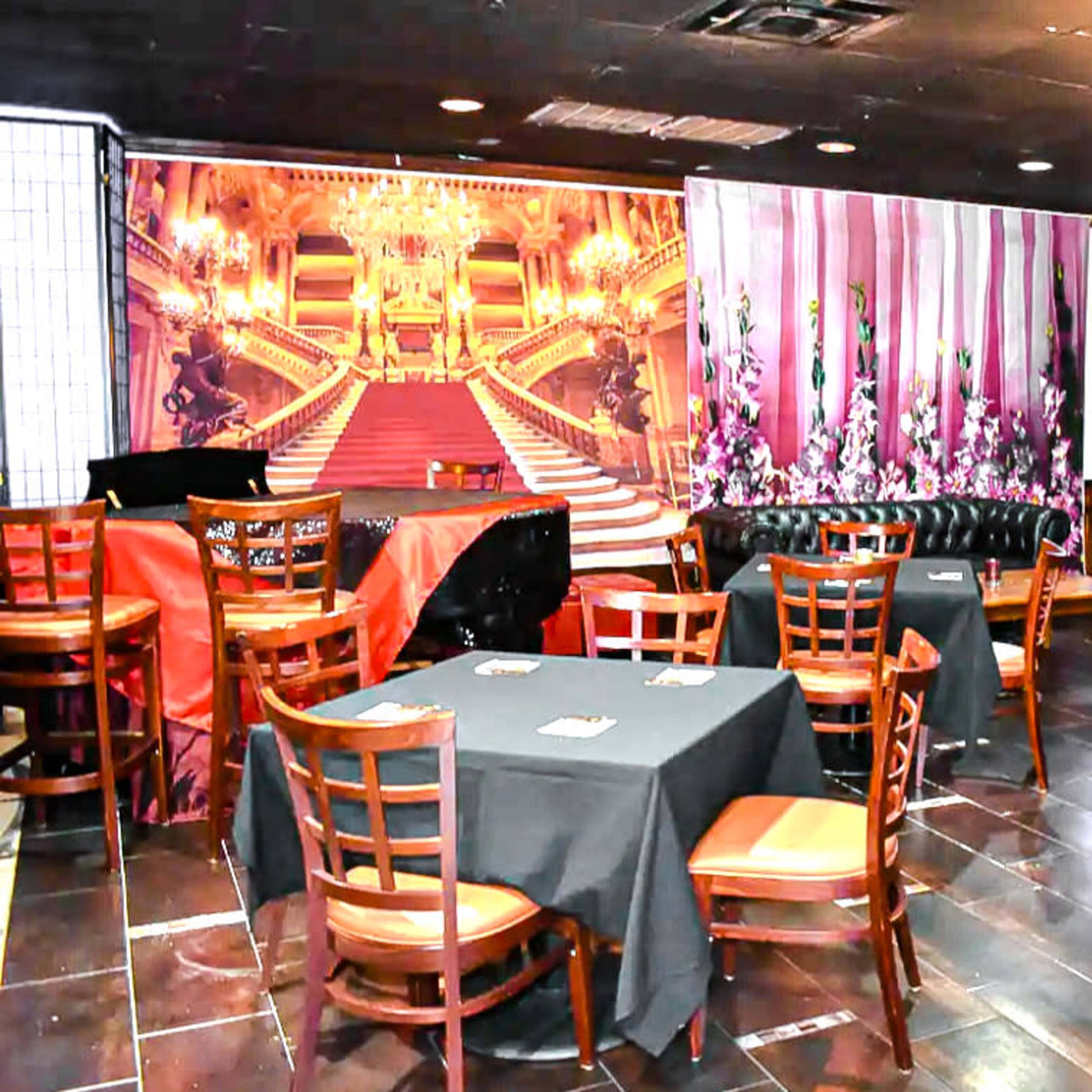 An empty restaurant with tables covered in black cloth and a large mural of an ornate staircase on the back wall.