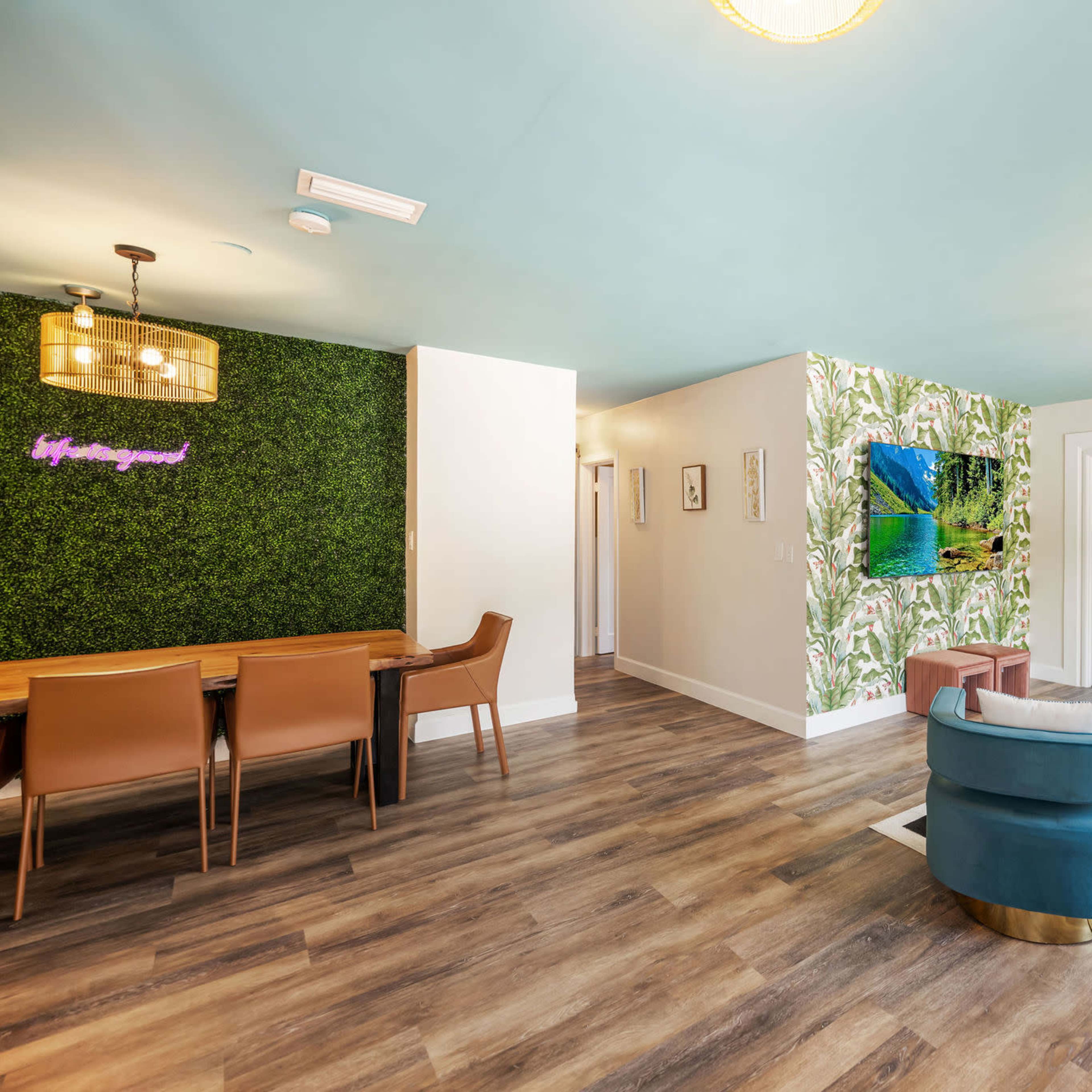 A modern living area with a green wall feature, a dining table, and decorative elements, including a large piece of artwork.
