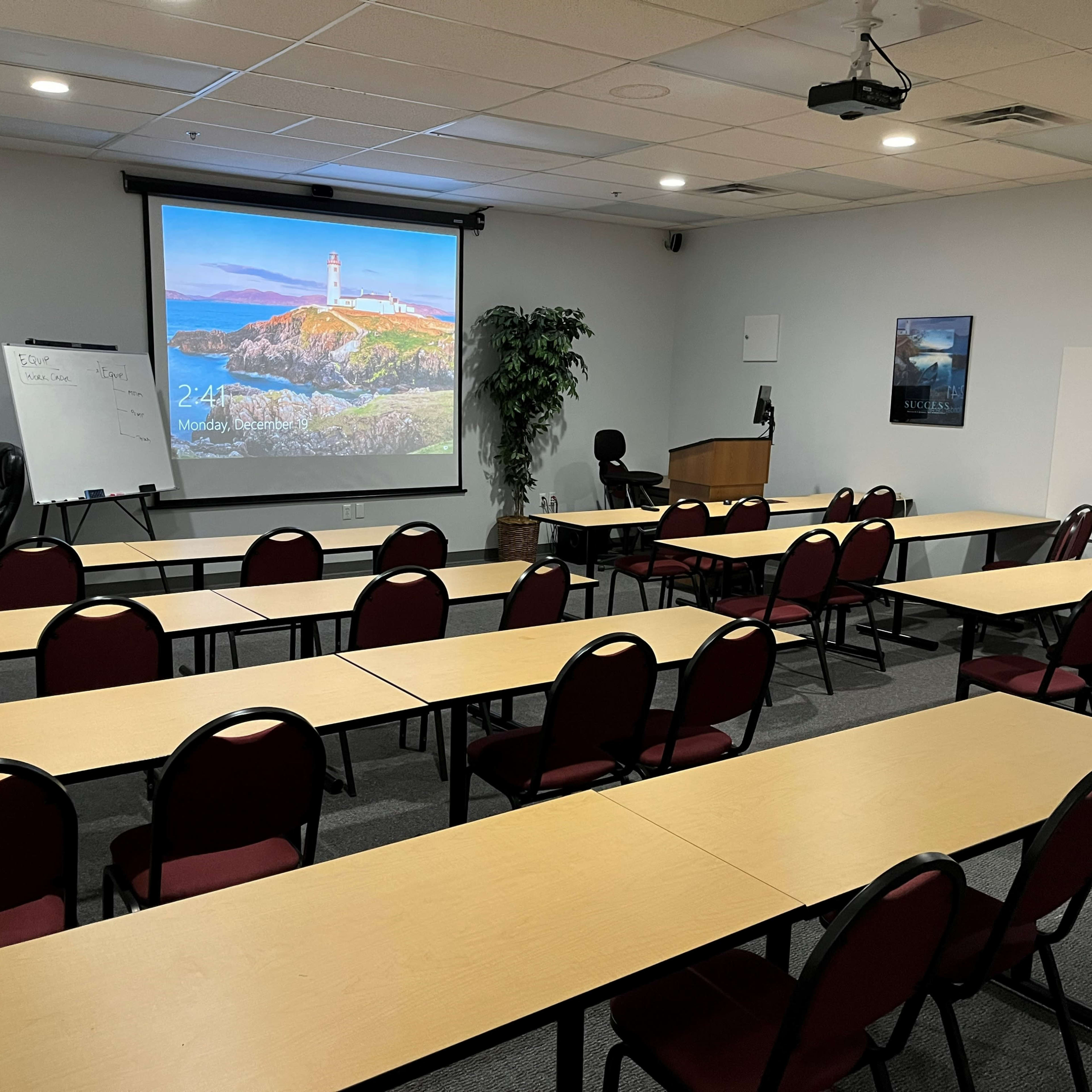 A conference room is set up with rows of tables and chairs, a projector screen displaying a lighthouse image, and a podium at the front.
