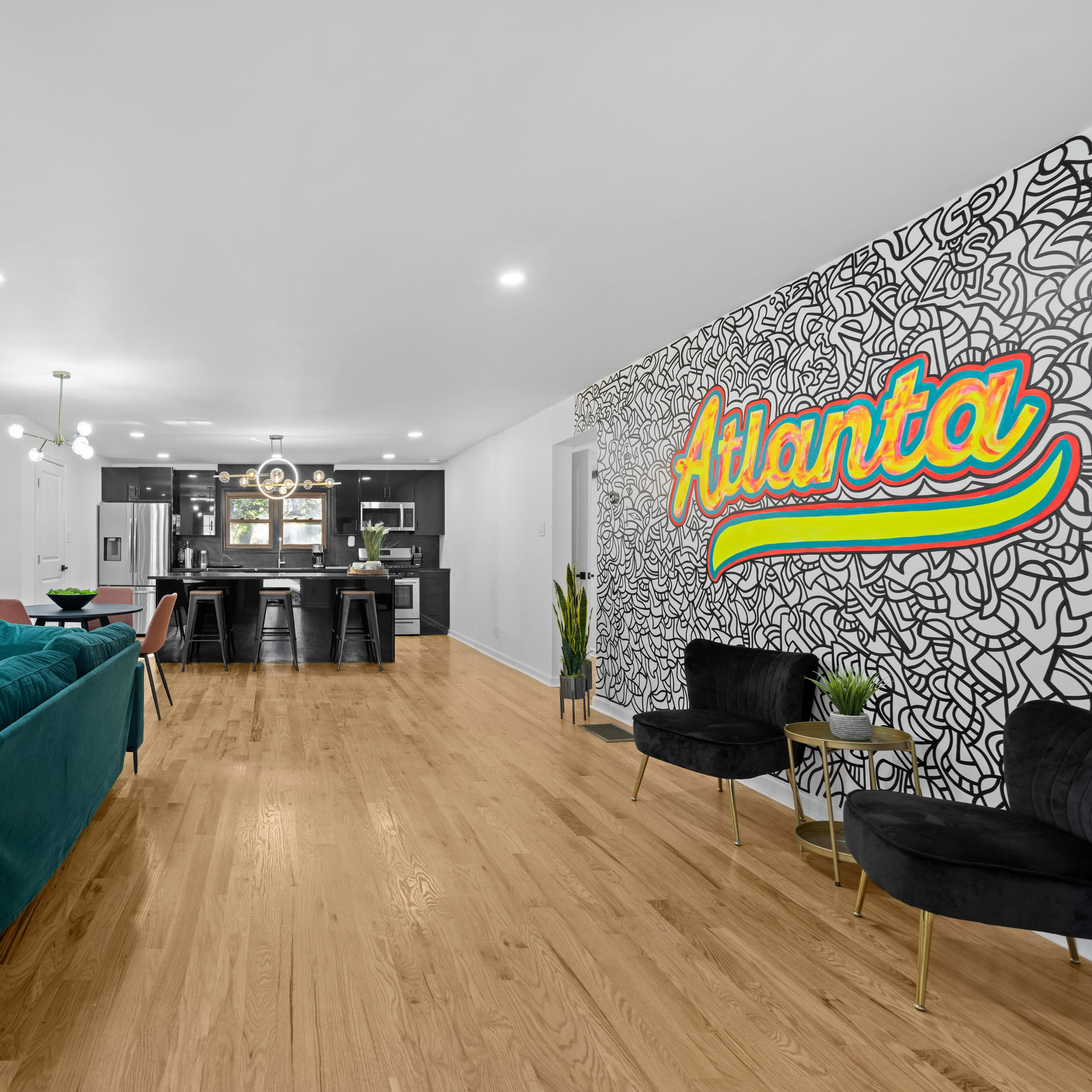 A spacious living area with a colorful mural reading "Atlanta," modern furniture, and a kitchen in the background.