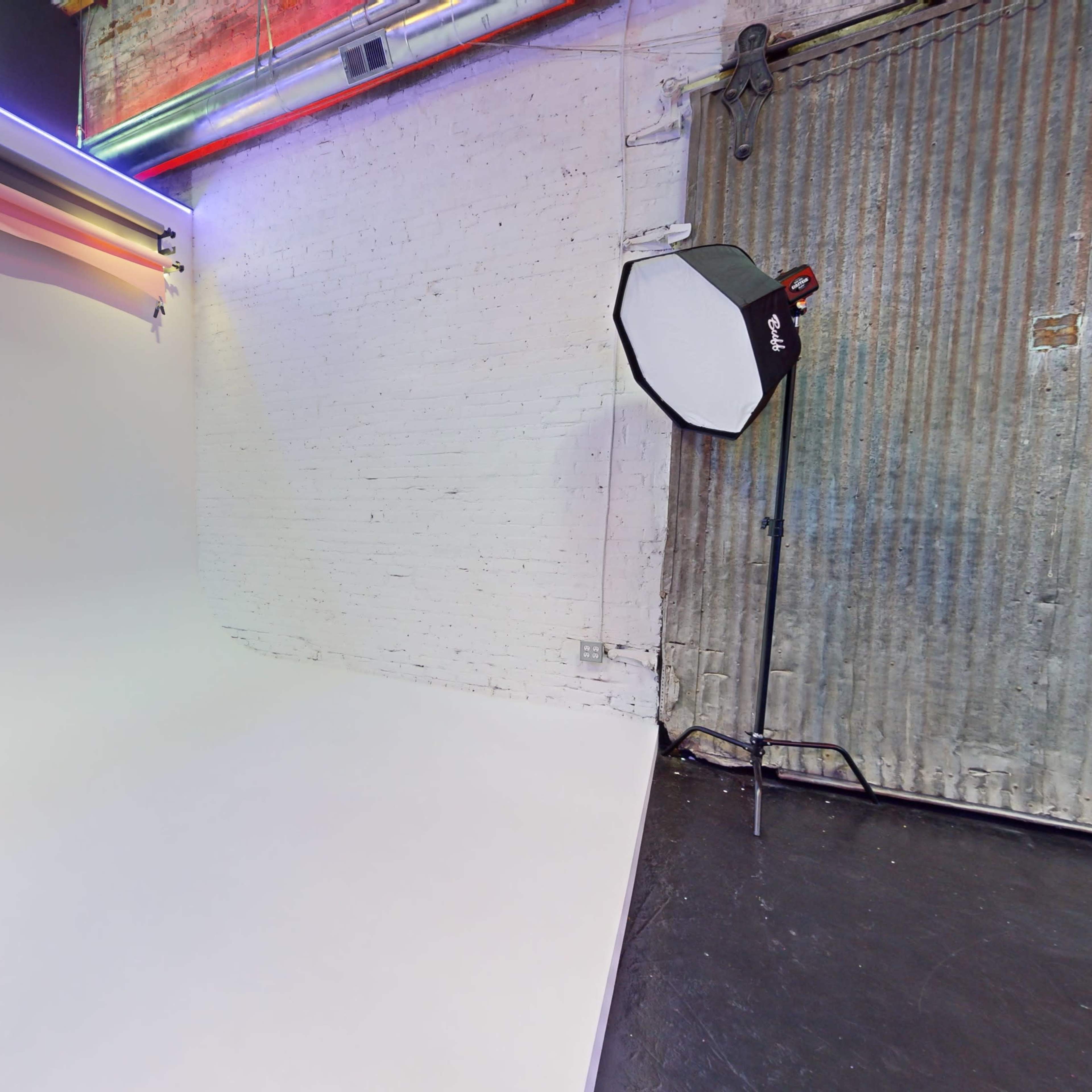 A photography studio with a seamless white backdrop and a softbox light positioned nearby against a textured wall.