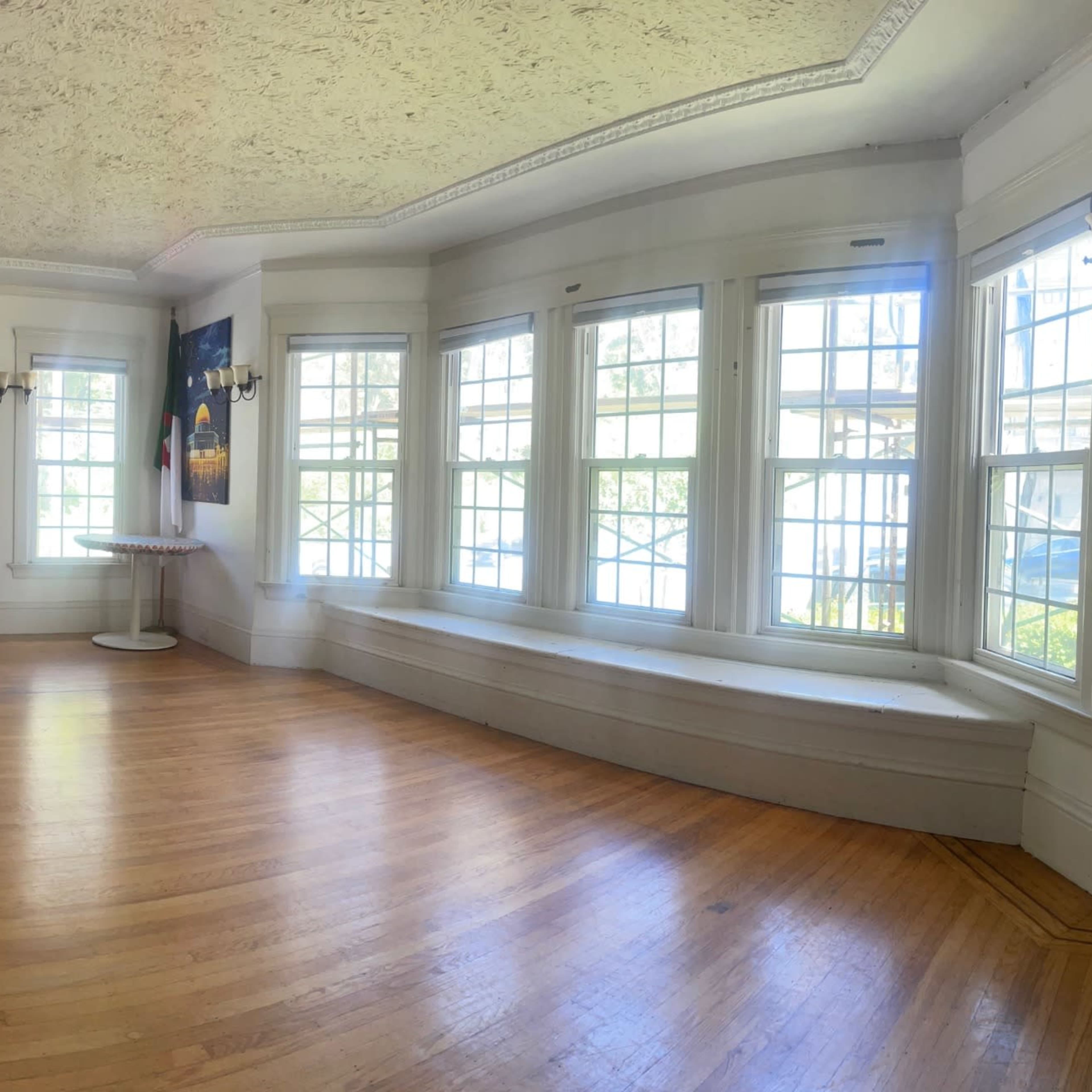 A panoramic view of a spacious room with wooden floors, large windows, and decorative wall art.