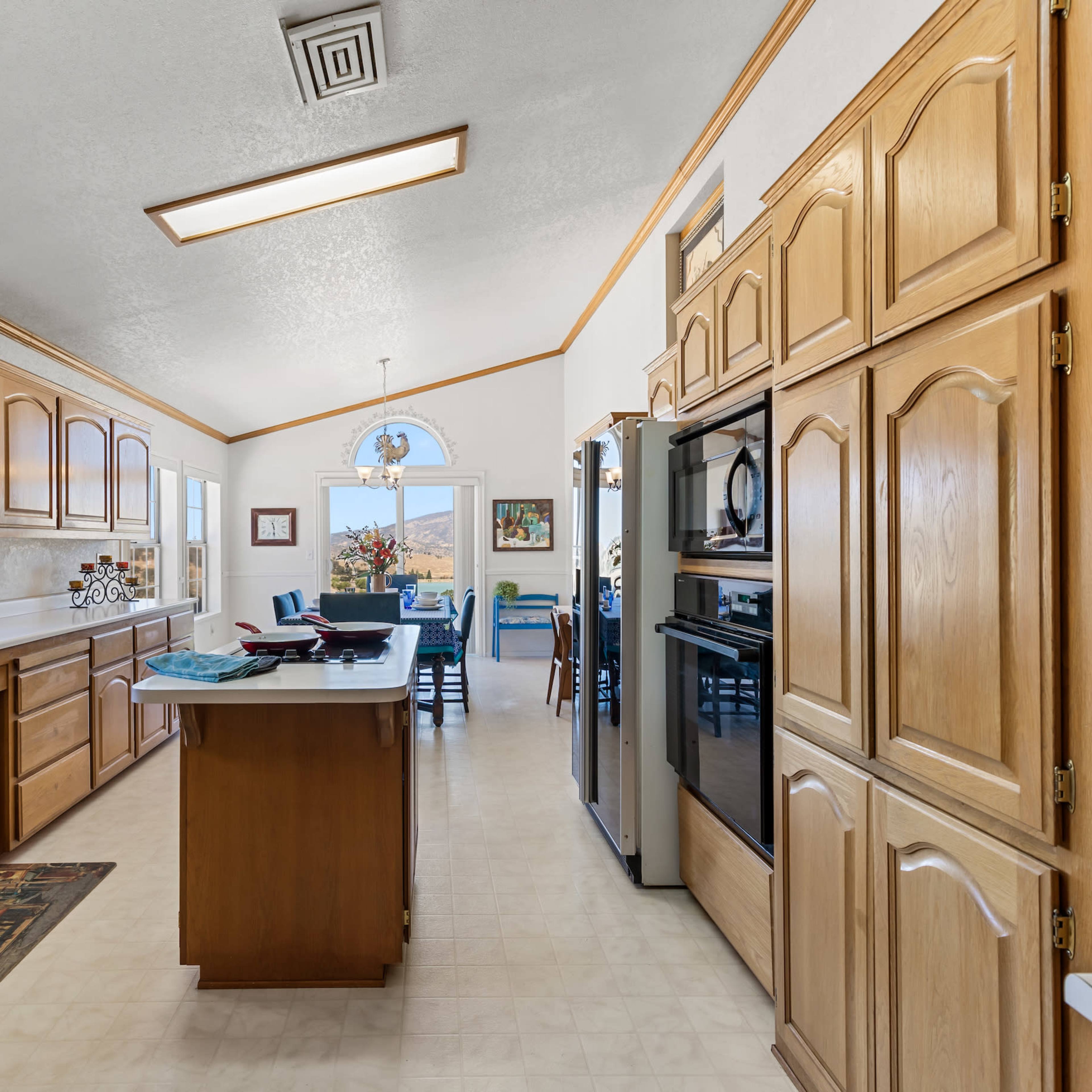 A spacious kitchen with wooden cabinets, a central island, and large windows allowing natural light to enter.