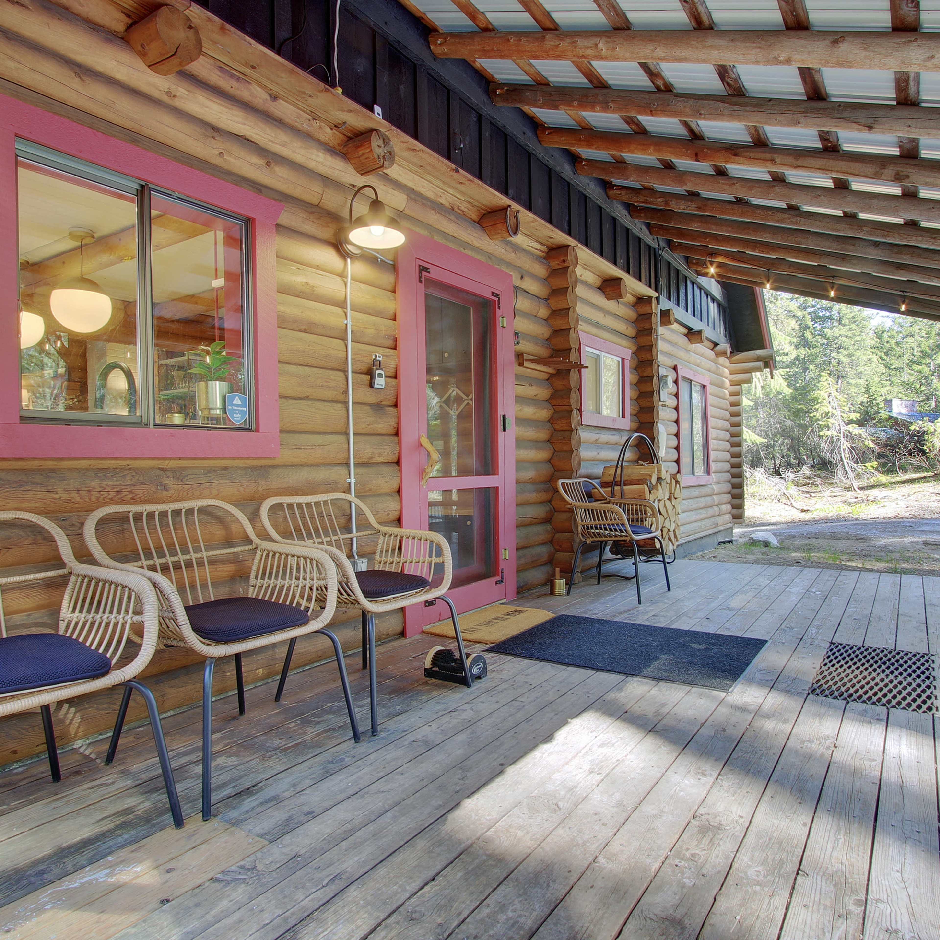 A wooden porch features several chairs and a door with a pink frame, surrounded by trees.