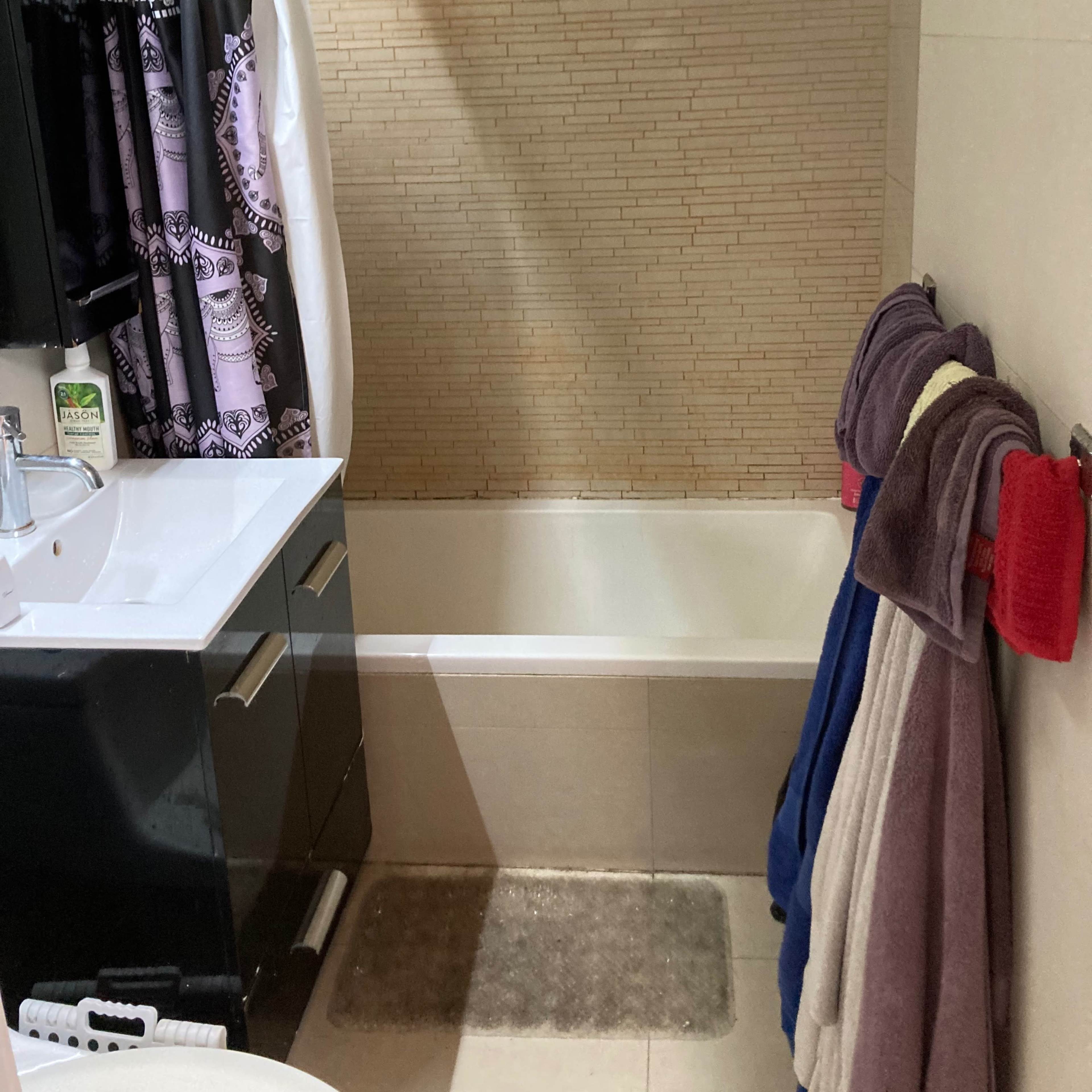 A small bathroom with a bathtub, a shower curtain, a sink with a cabinet, and several towels hanging on a rack.