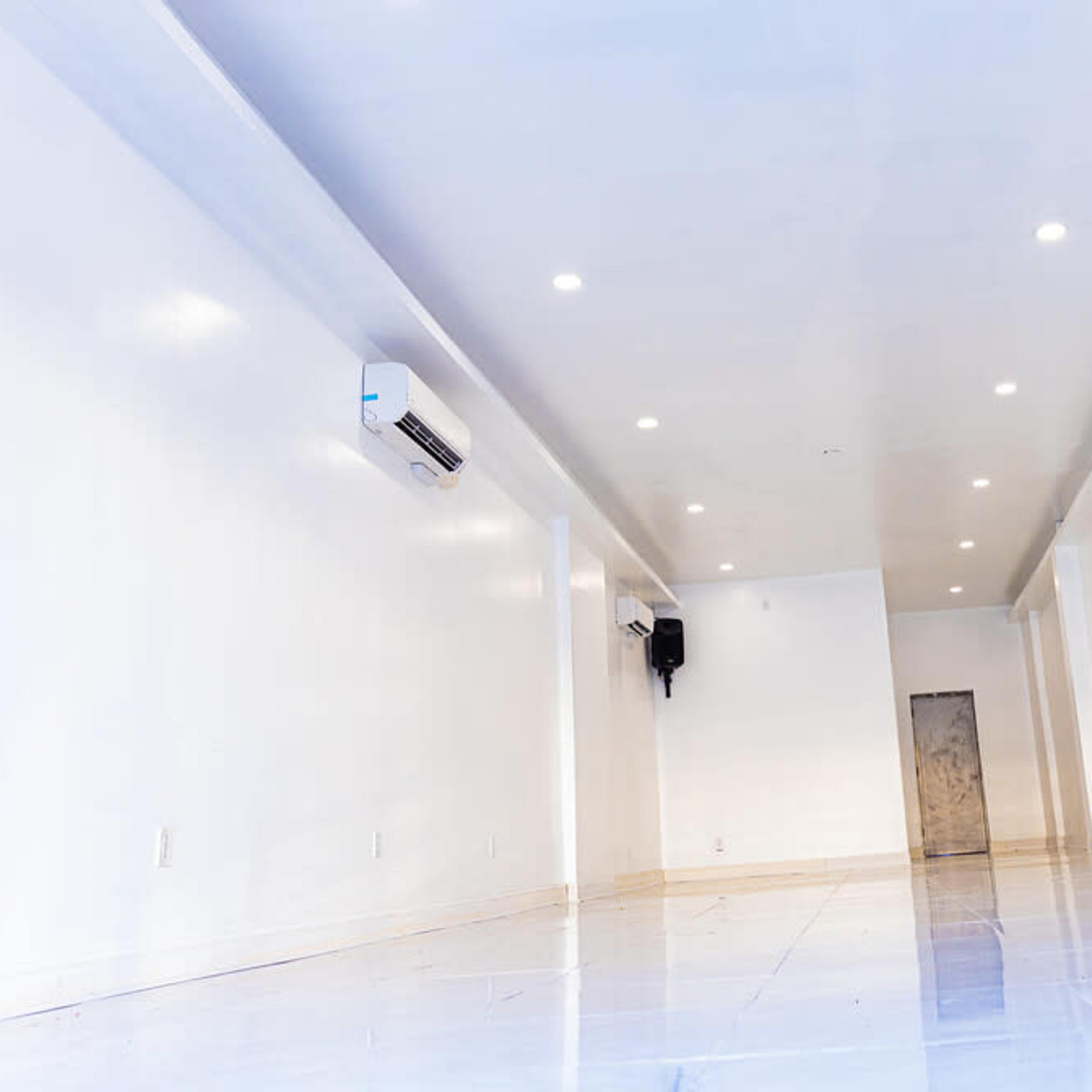 An empty room with white walls, a polished floor, and several overhead lights.