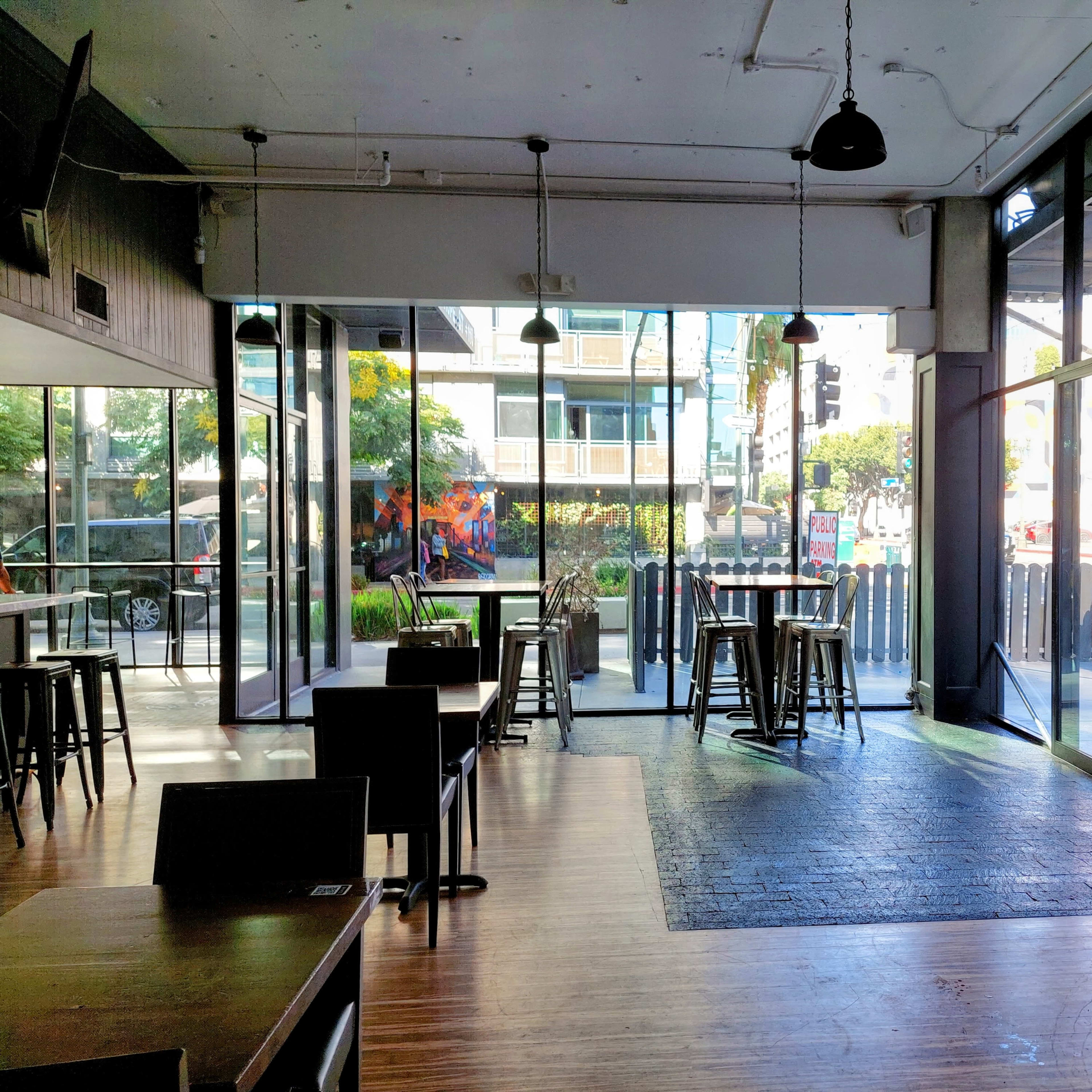 An empty café with large windows and a mix of high tables and chairs, allowing natural light to fill the space.