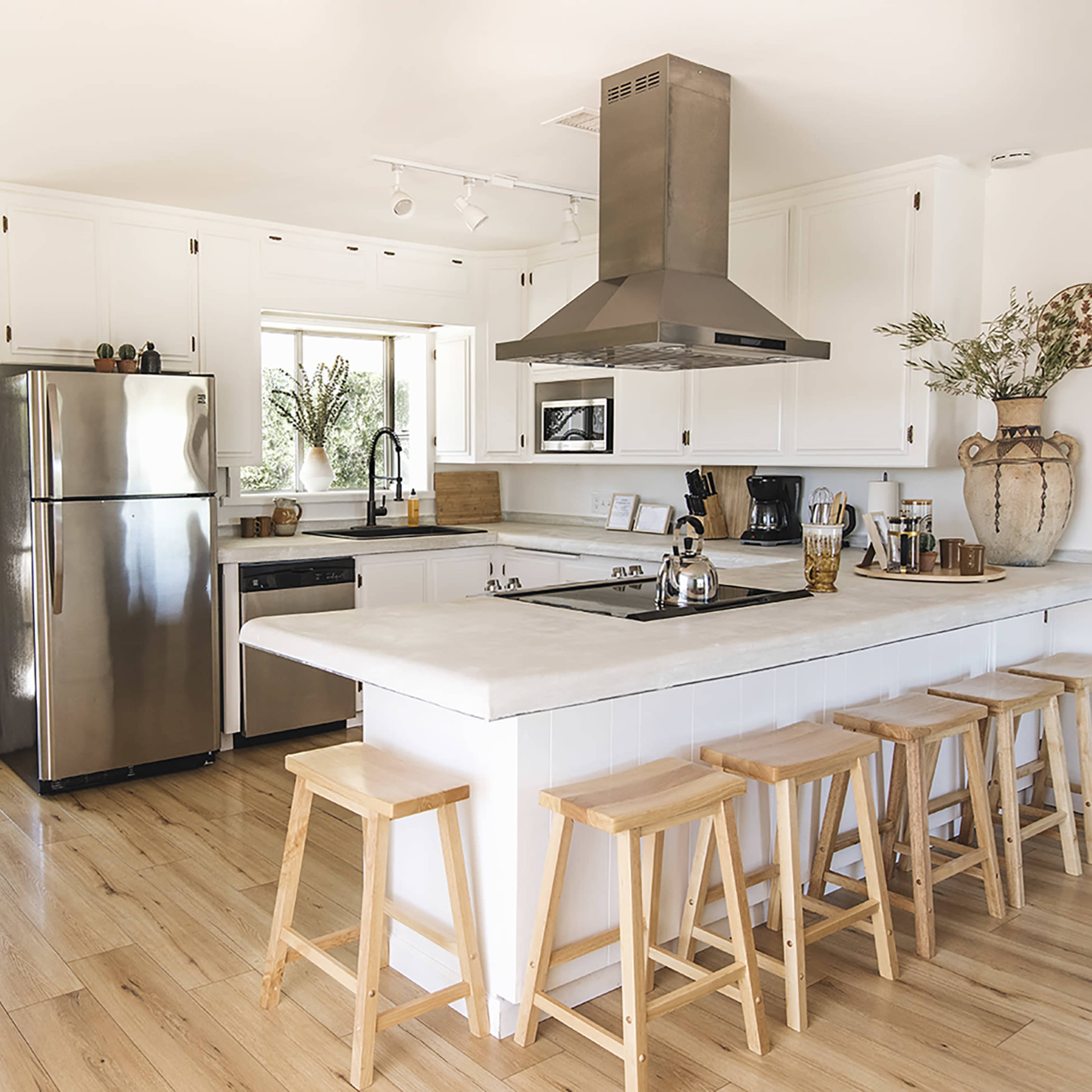 A modern kitchen features a stainless steel refrigerator, a countertop with bar stools, and a pendant hood over the stove.