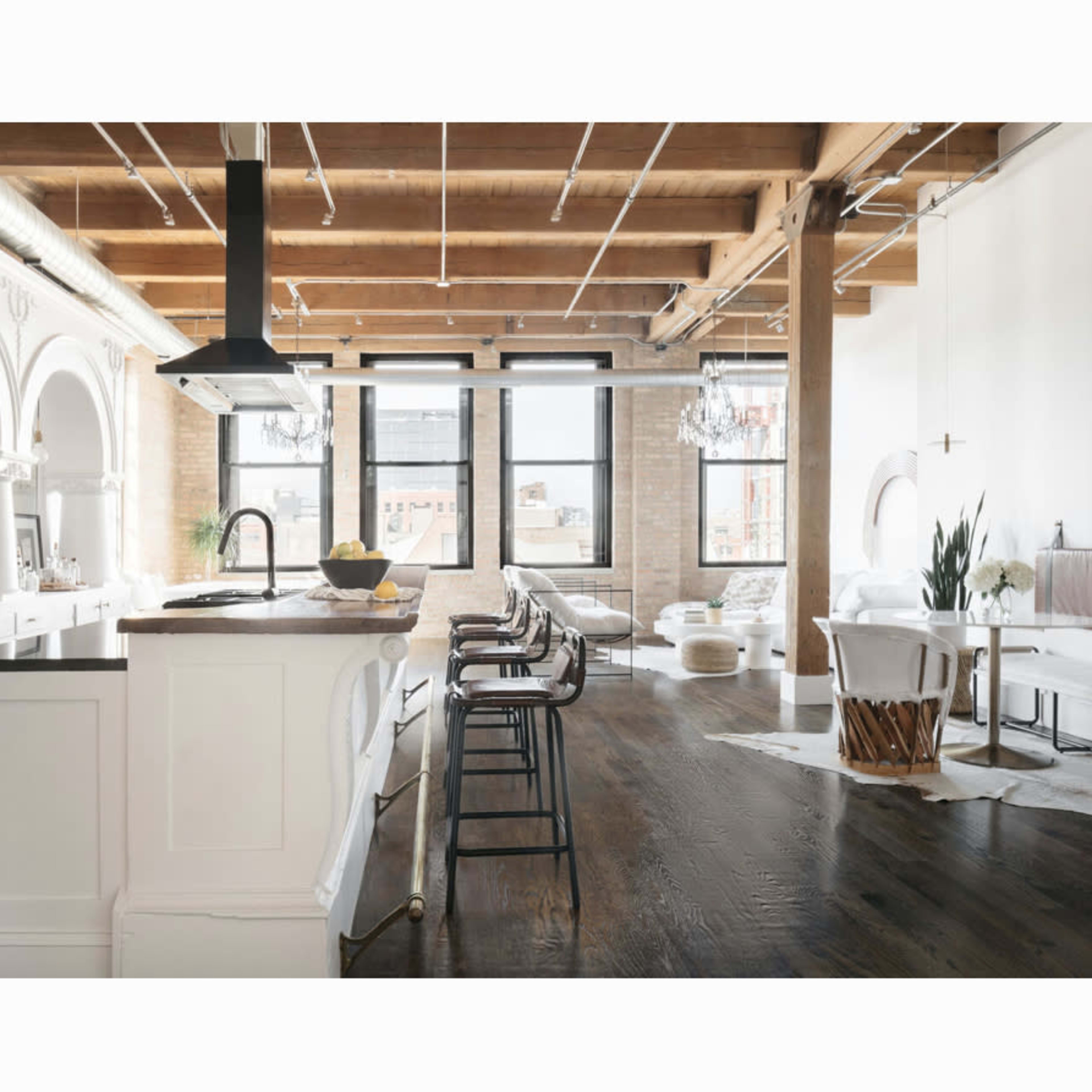 A spacious, modern loft features a kitchen island with bar stools, large windows allowing natural light, and a mix of seating areas.