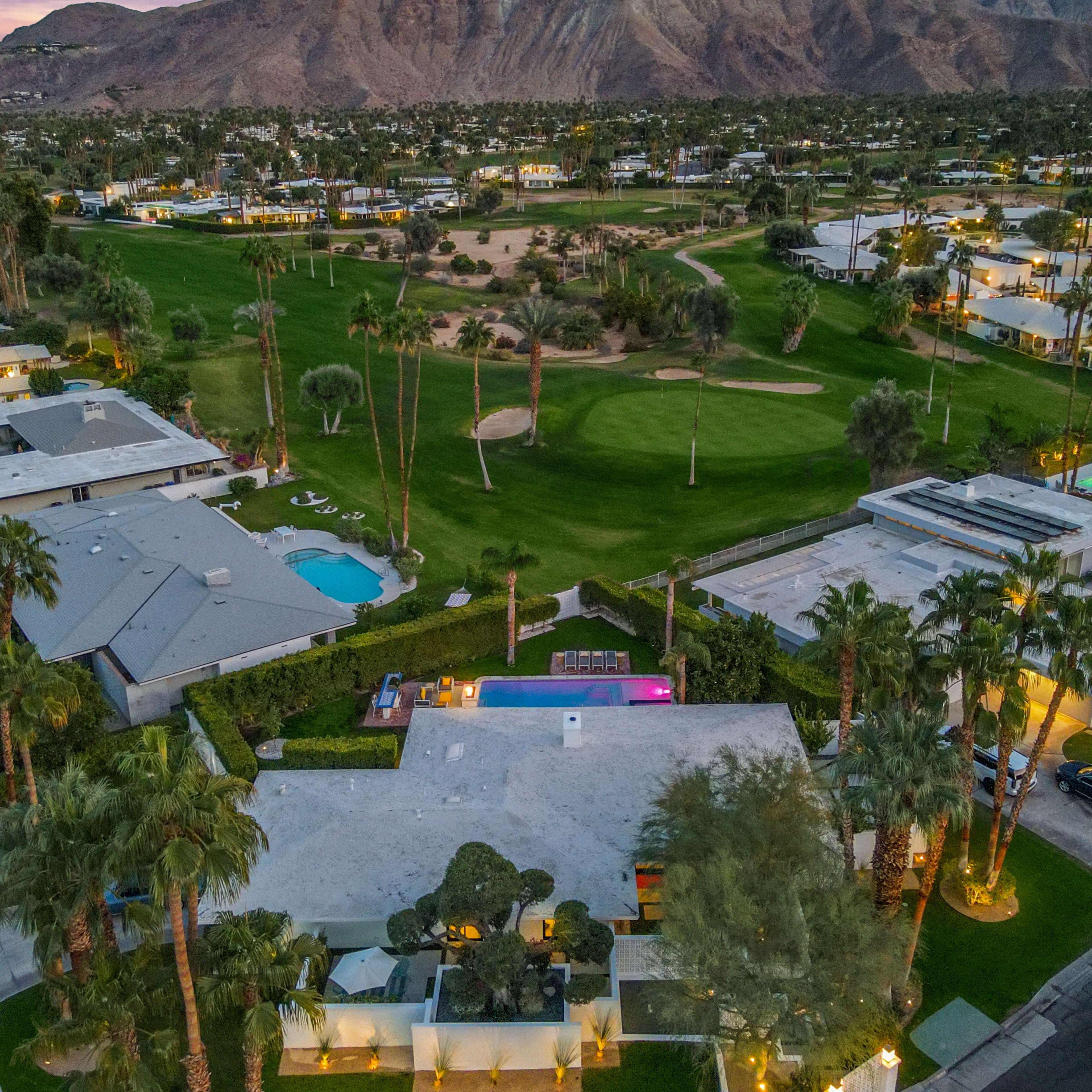 An aerial view of a golf course surrounded by residences, with palm trees and a swimming pool visible in the foreground.