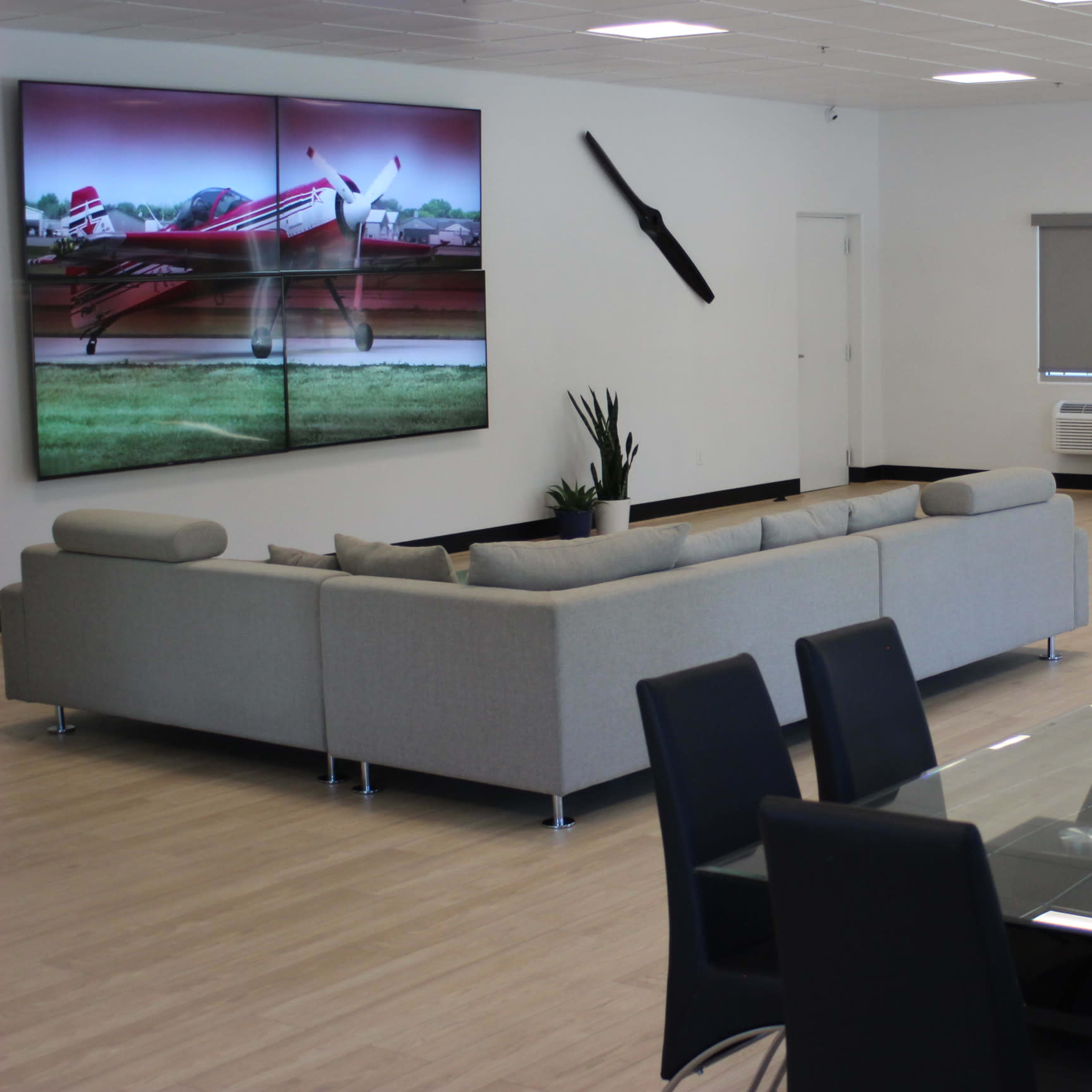 A modern interior space featuring a large sectional sofa, a glass dining table with black chairs, and a wall displaying a large digital artwork of an airplane.