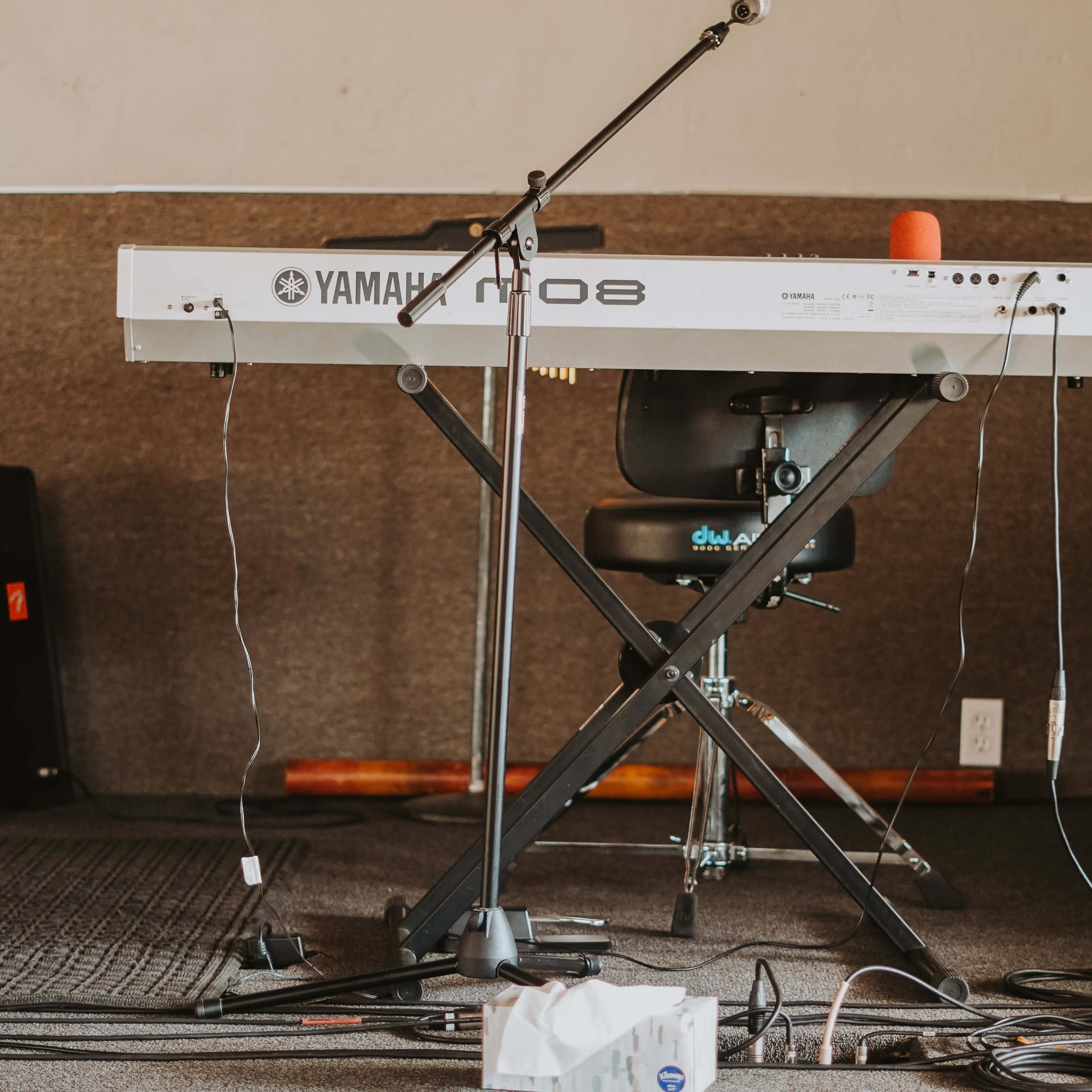 A Yamaha keyboard is set up on a stand, with cables strewn across the floor in a music practice room.