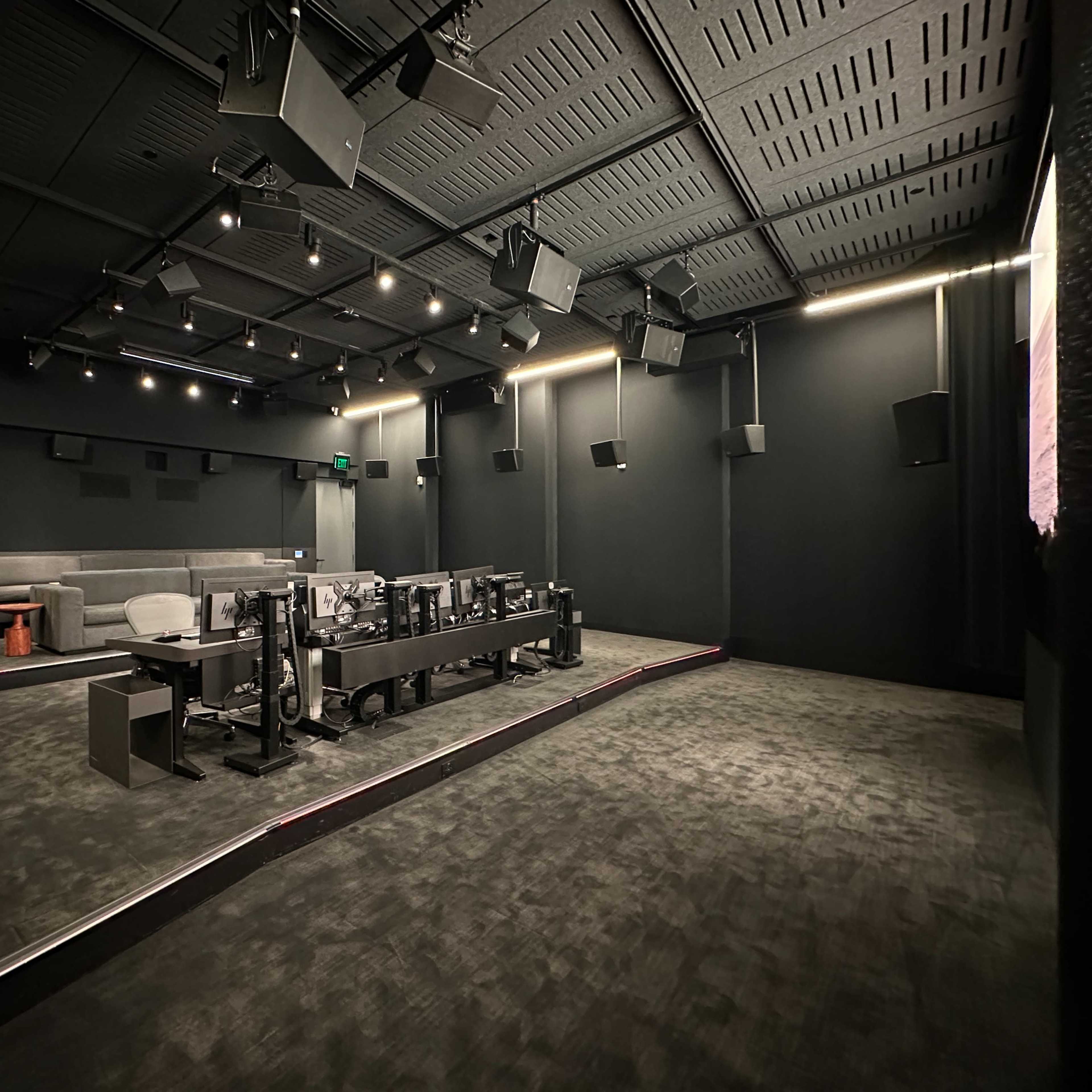 A dark, soundproofed studio room with multiple speakers, a long table with equipment, and a seating area.