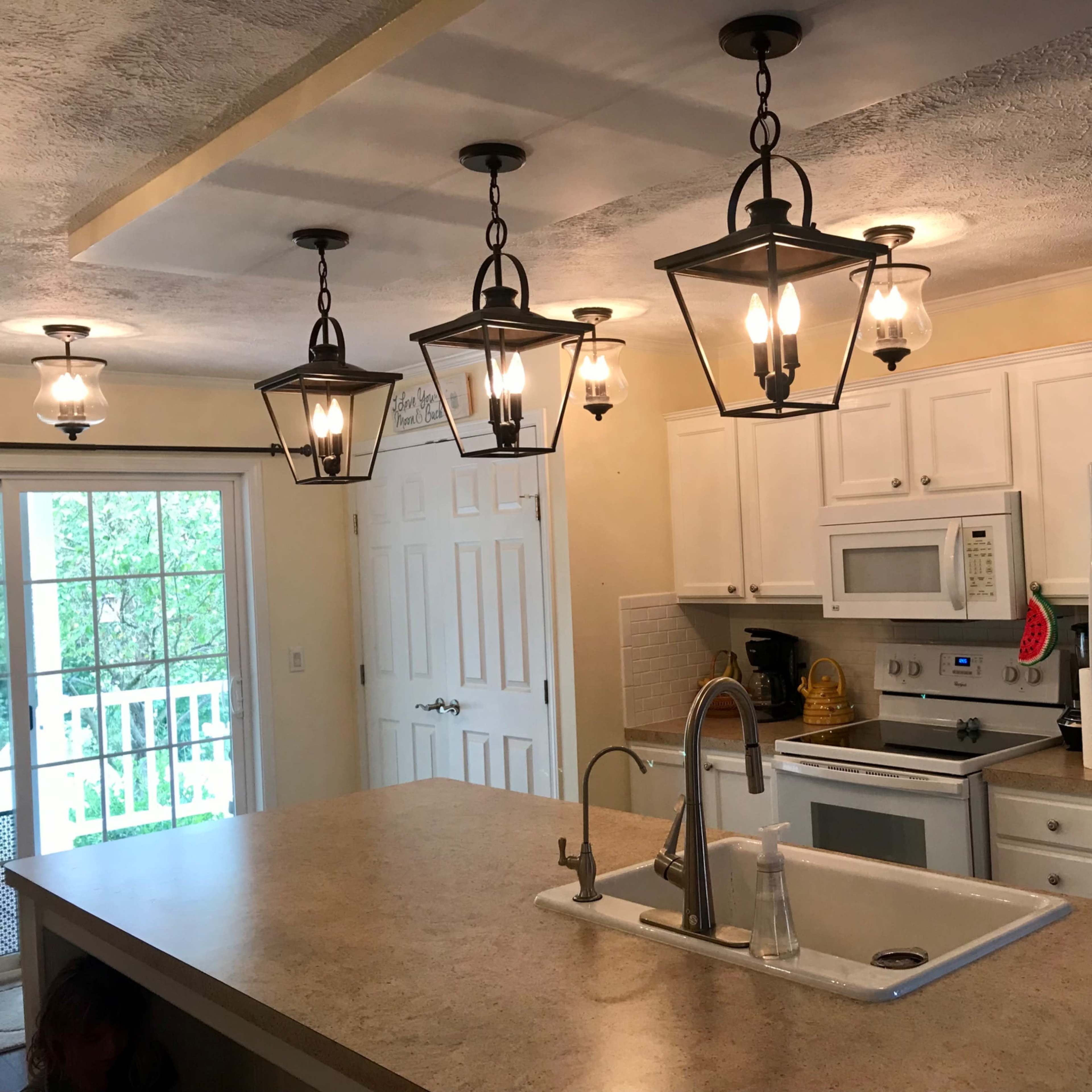A kitchen with white cabinets, a central island featuring a sink, and multiple pendant lights hanging from the ceiling.